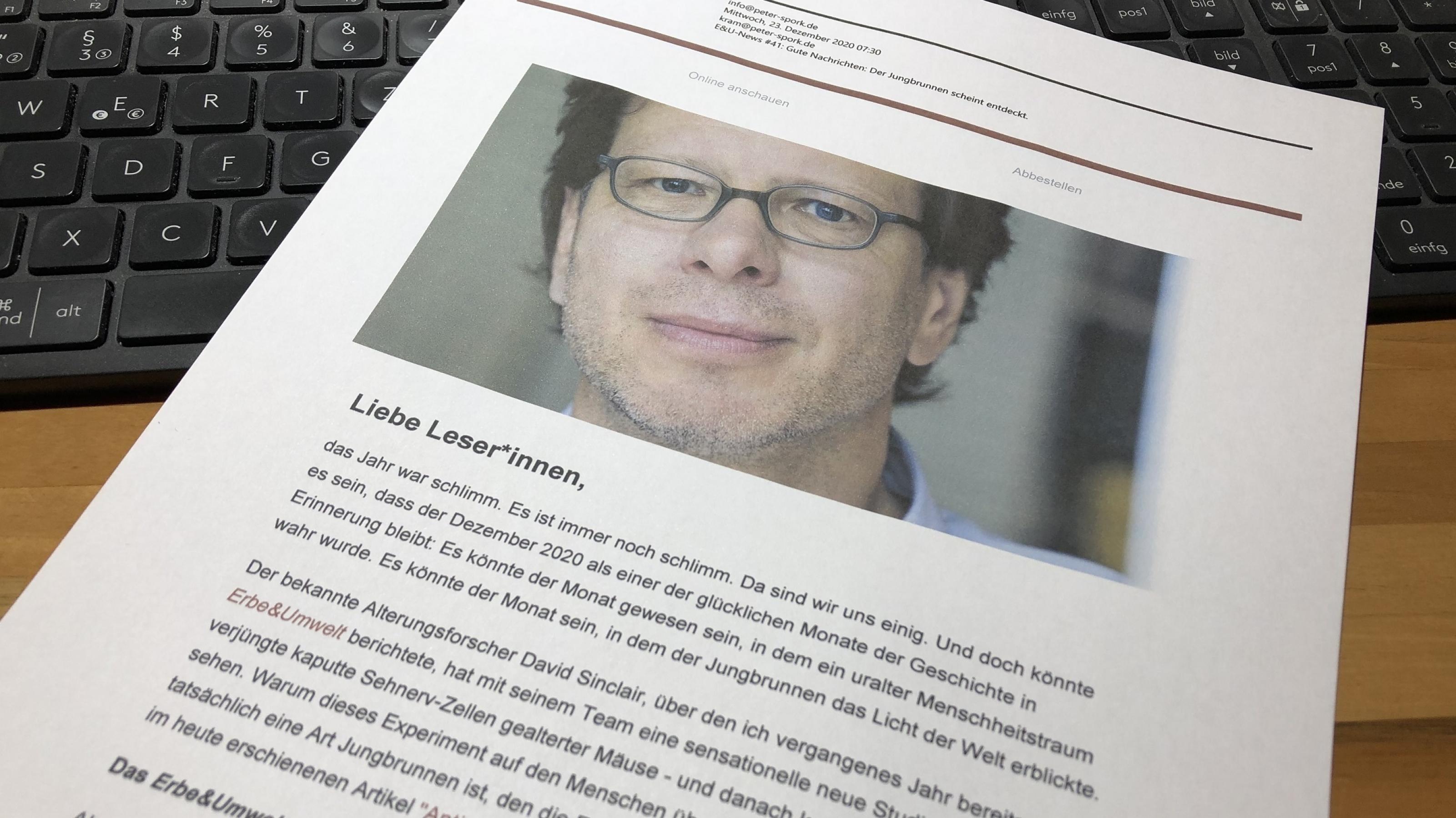 Die ausgedruckte Ausgabe der E&U-News liegt auf einem Schreibtisch: Oben ein Foto des Autors Dr. Peter Spork, darunter beginnt der Text, der formuliert ist wie ein Brief. Die ersten Worte sind: Liebe LeserInnen, …