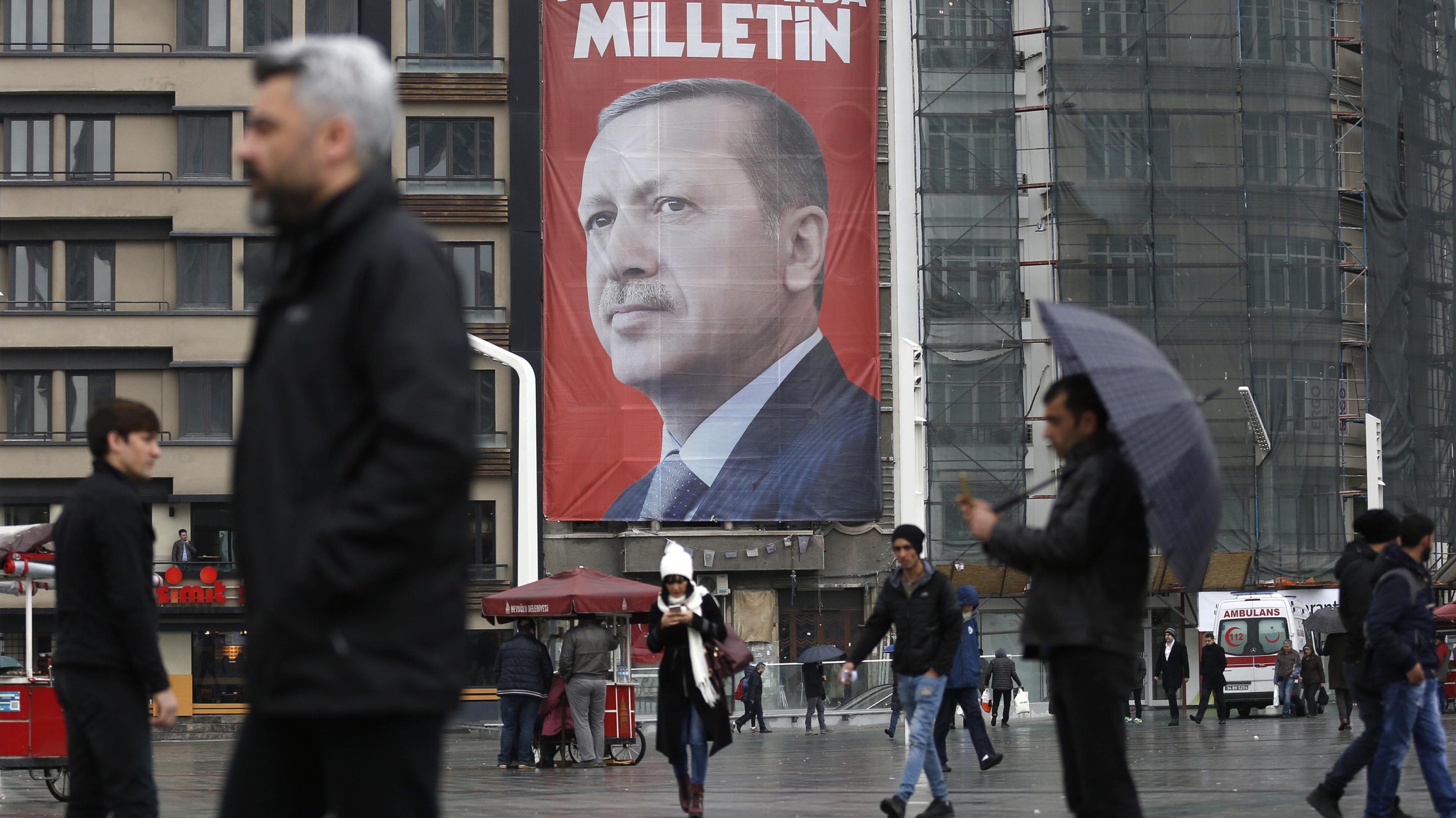 Menschen auf einem Platz vor einem Gebäude mit einem großen Plakat, das Erdogan zeigt.