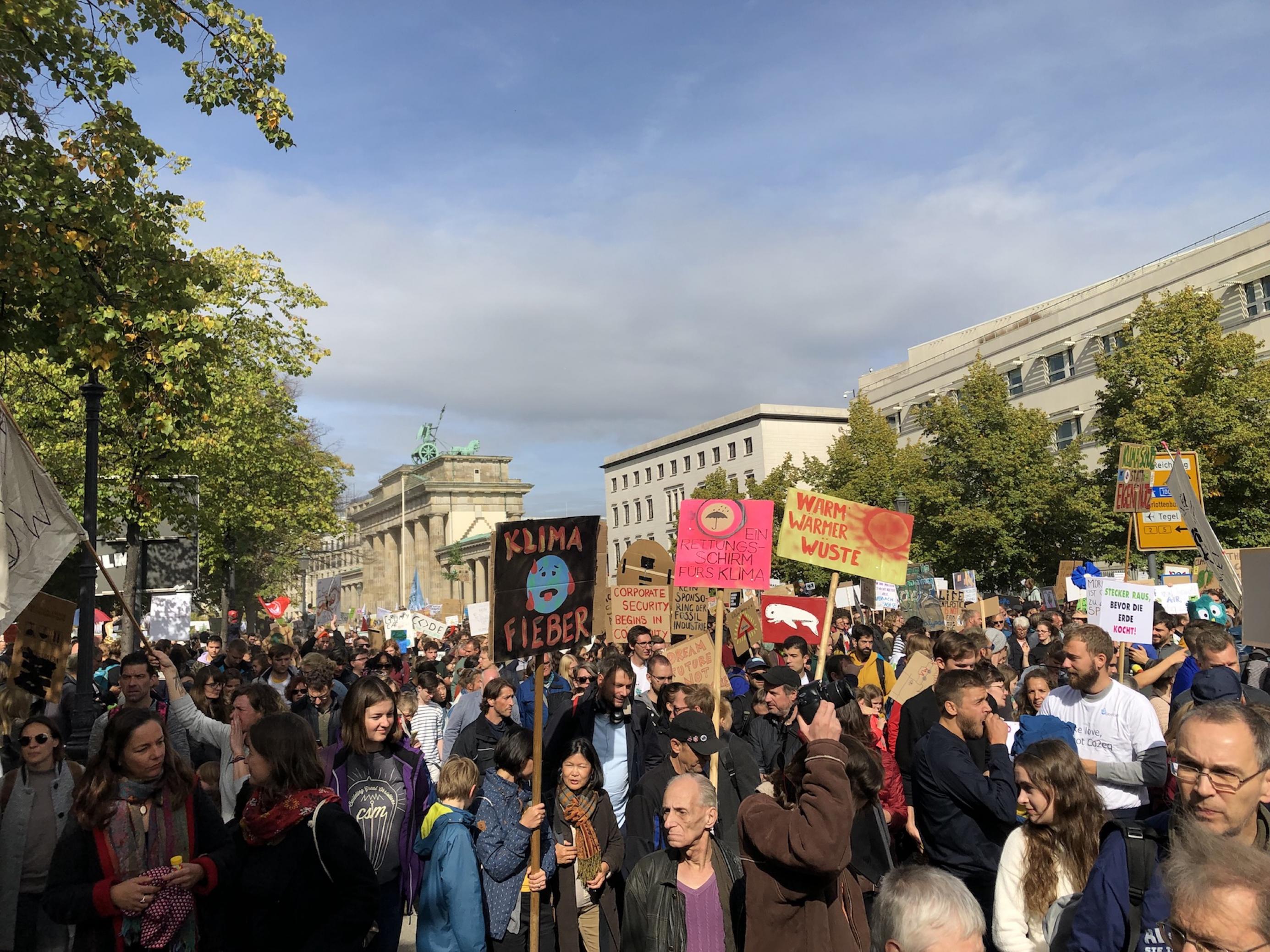 Demonstranten der Bewegung „Fridays for Future“ ziehen am Brandenburger Tor vorbei. Sie halten Plakate hoch, auf denen unter anderem „Klima Fieber“ steht