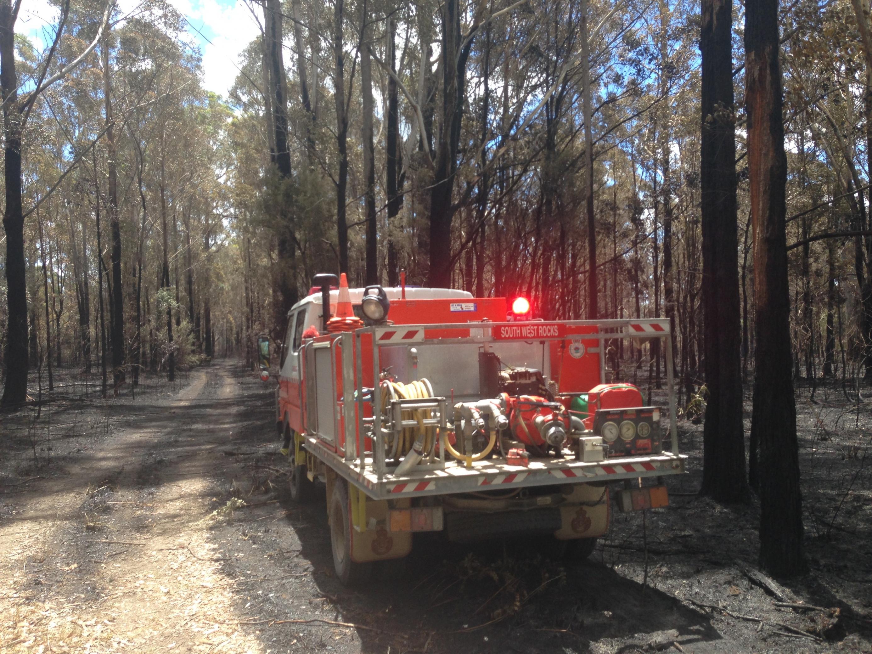 Ein Löschfahrzeug parkt zwischen schwarzen, verbrannten Baumstämmen in einem Waldstück in New South Wales. Die Feuerwehrleute begutachten den Schaden und checken ob es Spotfires gibt.