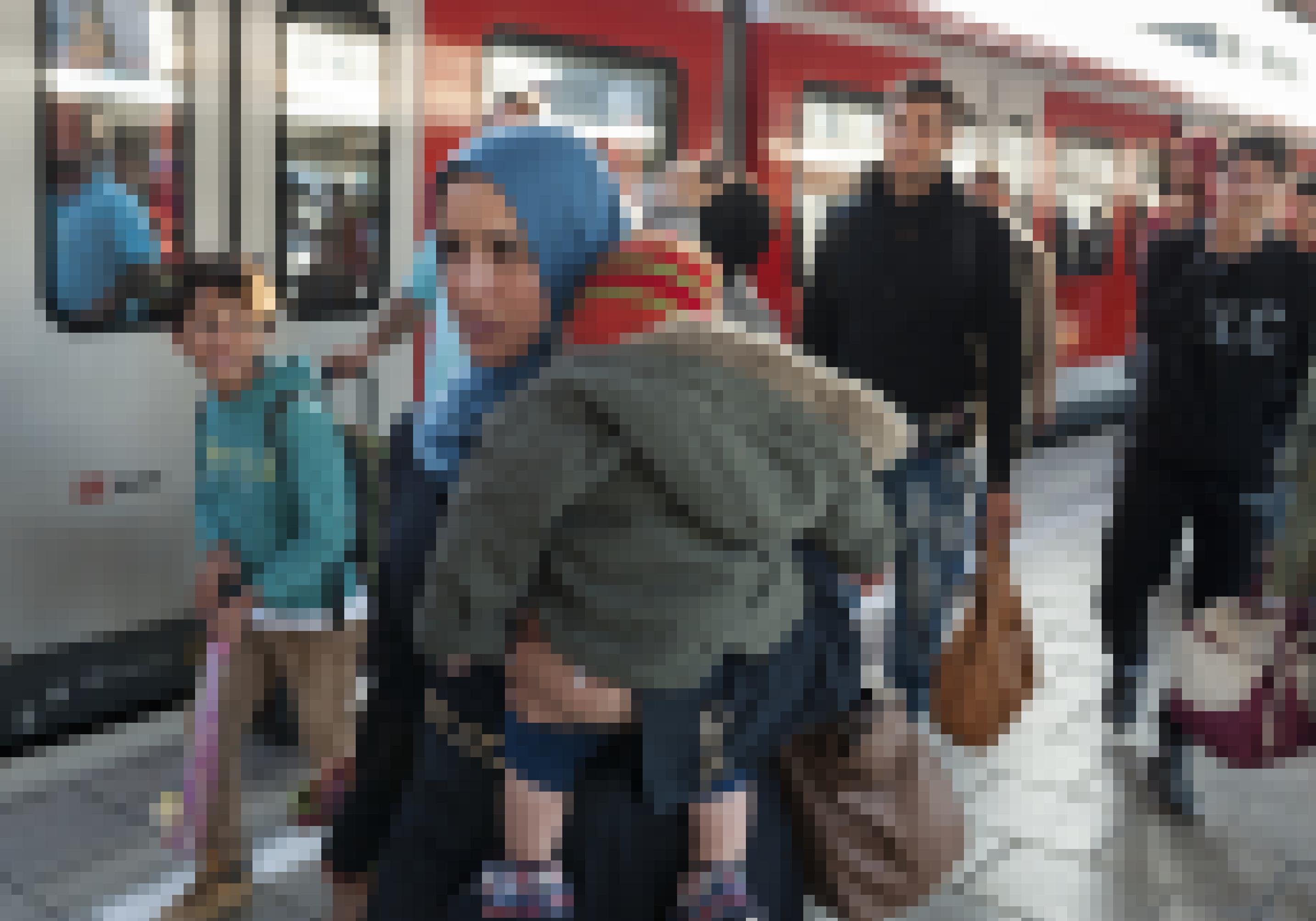 Eine Frau mit Kopftuch und einem Kleinkind auf dem Arm geht auf einem Bahnsteig. Im Hintergrund sind weitere Menschen zu sehen.