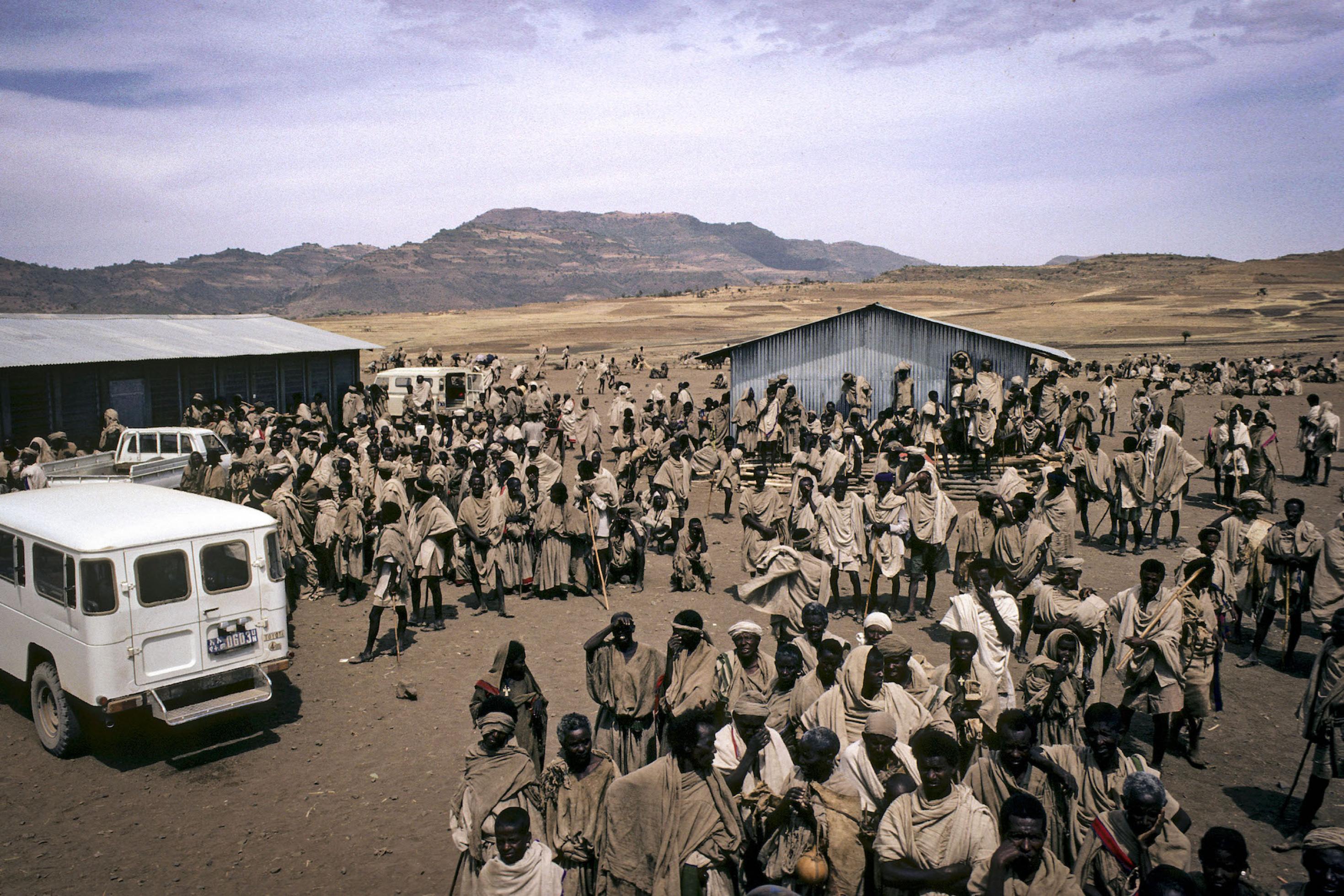 In einer Wüstenlandschaft in Äthiopien, vor Wellblechhütten und Geländerwagen warten 1983 die Bewohner des Ebinat-Lagers auf Hilfe durch UN-Mitarbeiter. Die seit Jahrzehnten bekannten Probleme von regionalen Konflikten und Hungersnöten könnten sich in den kommenden Dekaden zuspitzen, warnen Klimaforscher.