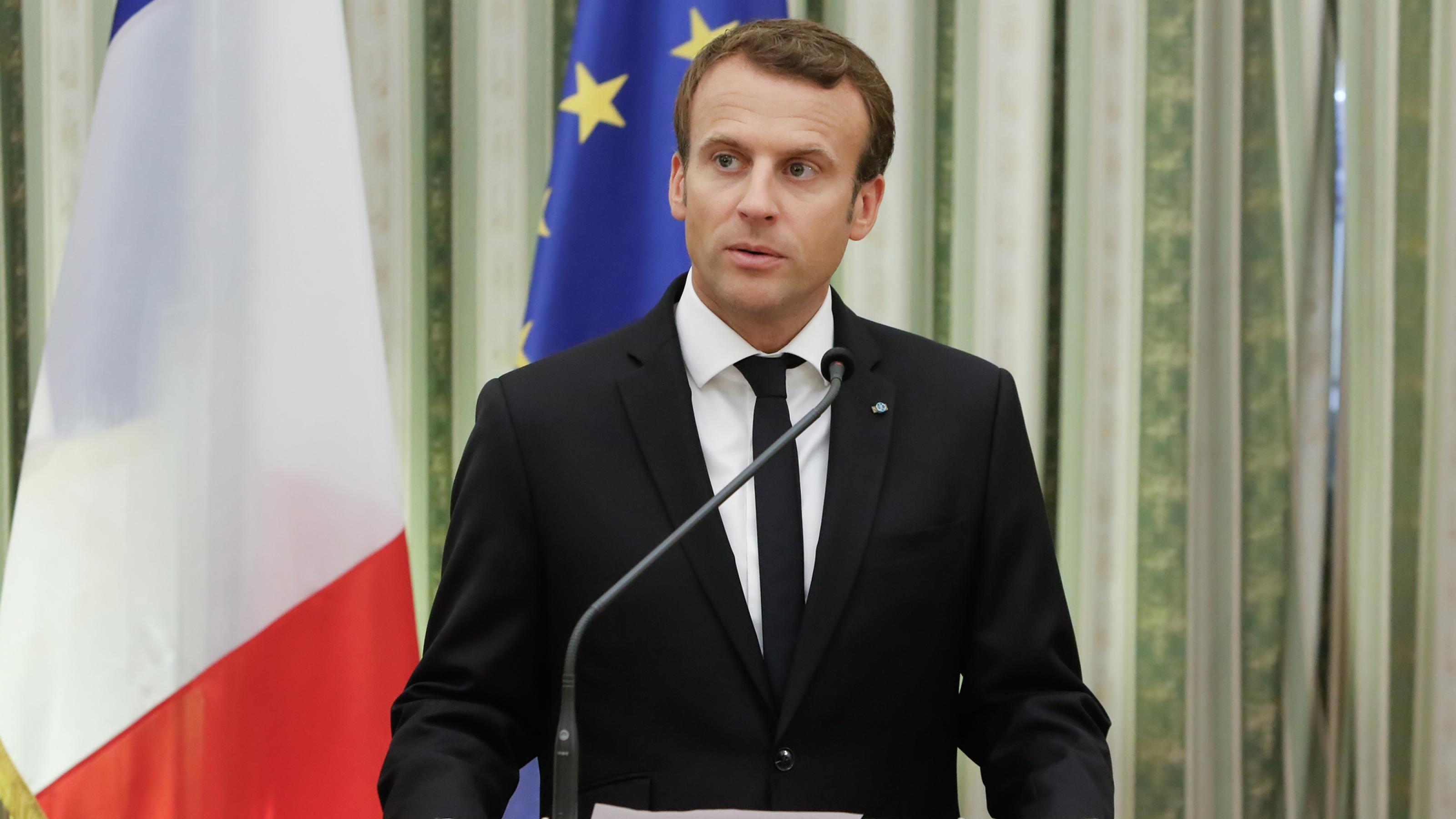Emmanuel Macron an einem Rednerpult, die griechische und die Europaflagge im Hintergrund
