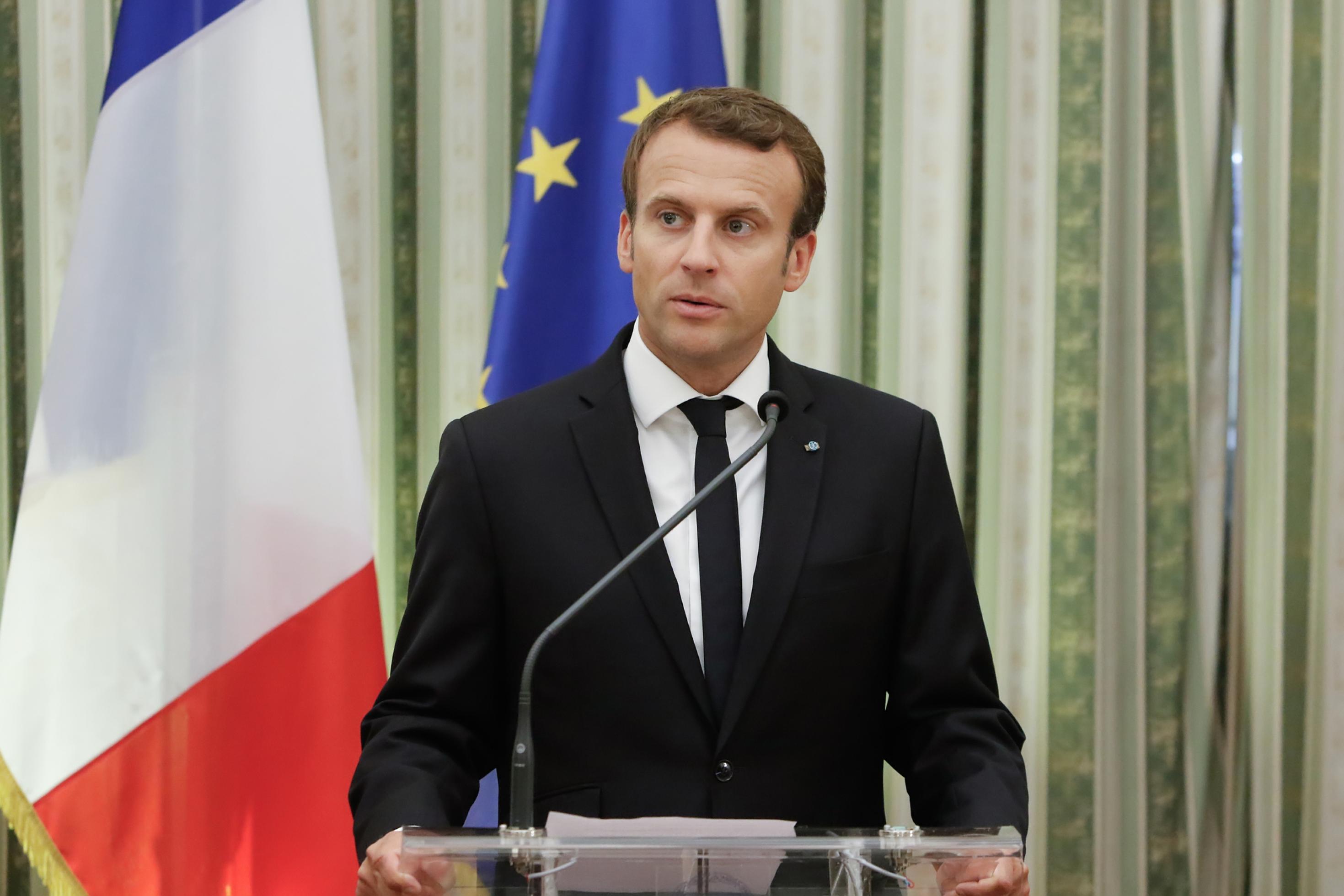 Emmanuel Macron an einem Rednerpult, die griechische und die Europaflagge im Hintergrund