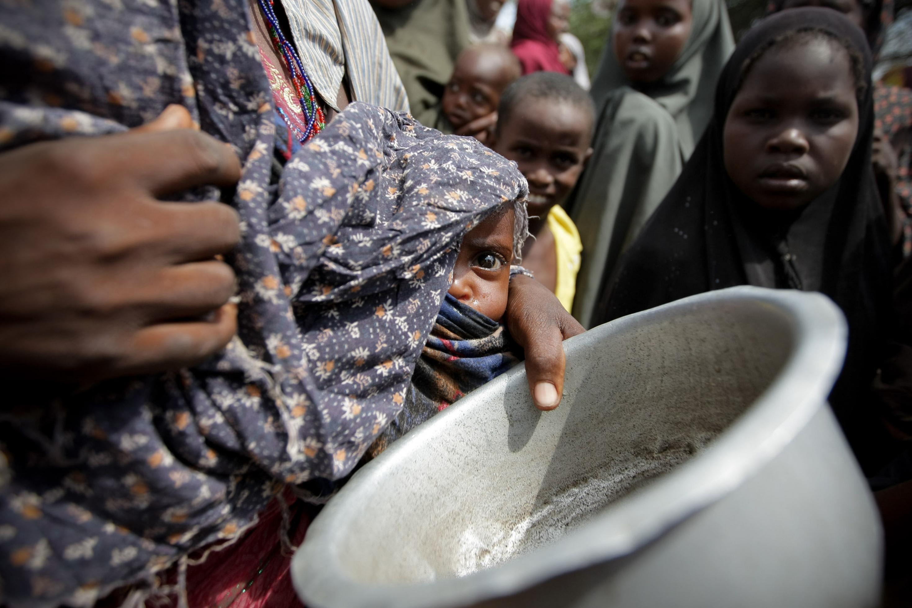 Eine Frau mit ihrem unterernährten Baby steht im Jahr 2011 im somalischen Flüchtlingslager Badbado nach Essen an. Man sieht nur einen Ausschnitt von ihrer Körpermitte. Sie trägt ein kleines Kind an der Hüfte, das unter einem Tuch hervorblickt. Die Mutter hat eine Blechschüssel in der Hand. Im Hintergrund stehen andere Menschen. –
Bilder solchen Elends rühren Menschen vielleicht zu Spenden für Hungernden in Afrika, aber als Symbolbild des Klimawandels taugen sie wenig: zu weit weg vom Alltag sind die Betroffenen, zu wenig drängt sich dem Betrachter auf, dass die Veränderung der Muster des Wetters entscheidend zur Not auf den fremden Kontinent beiträgt.
