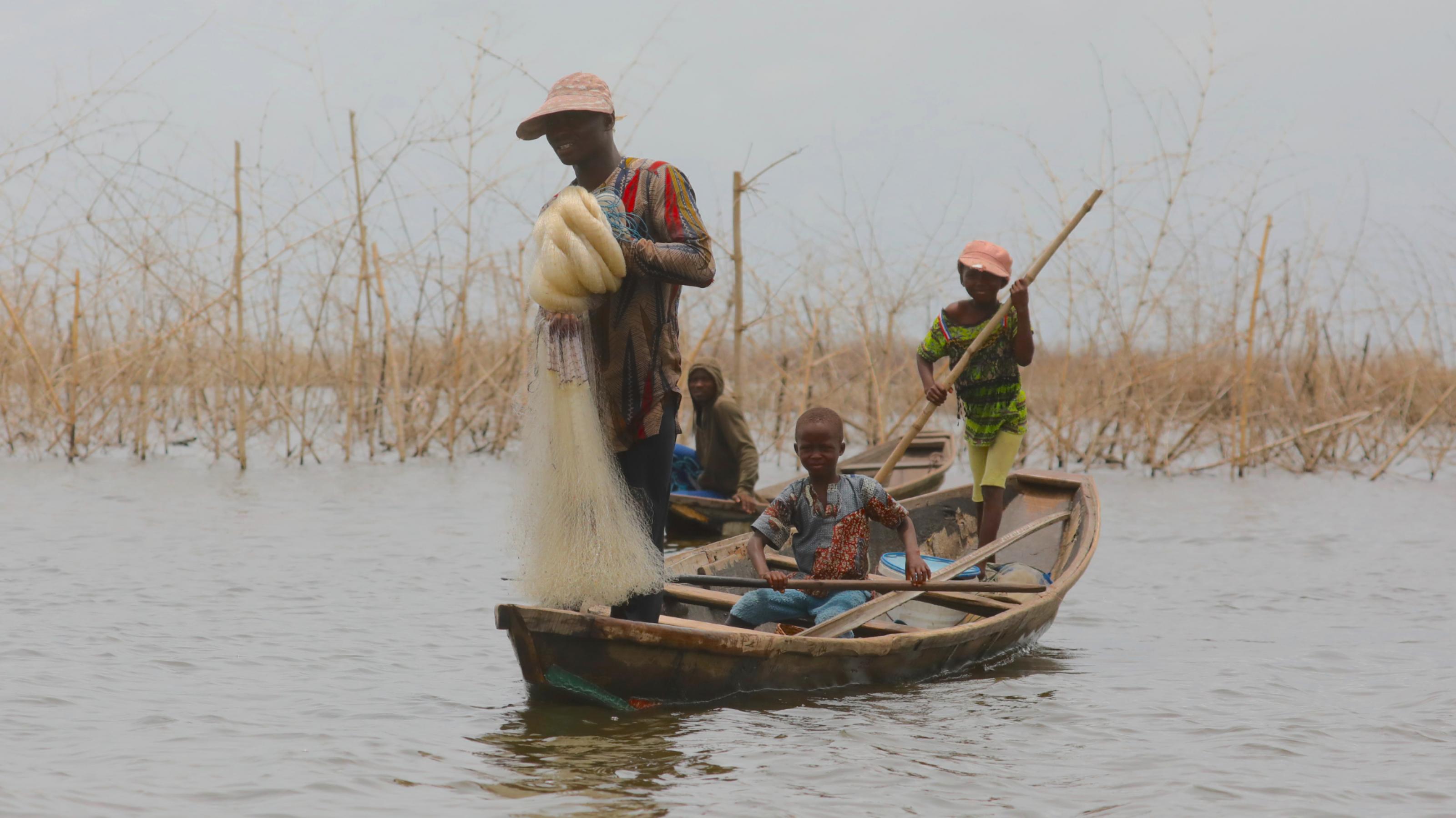 Ein Boot mit Vater und Sohn, der Vater hält ein Fischernetz in der Hand.