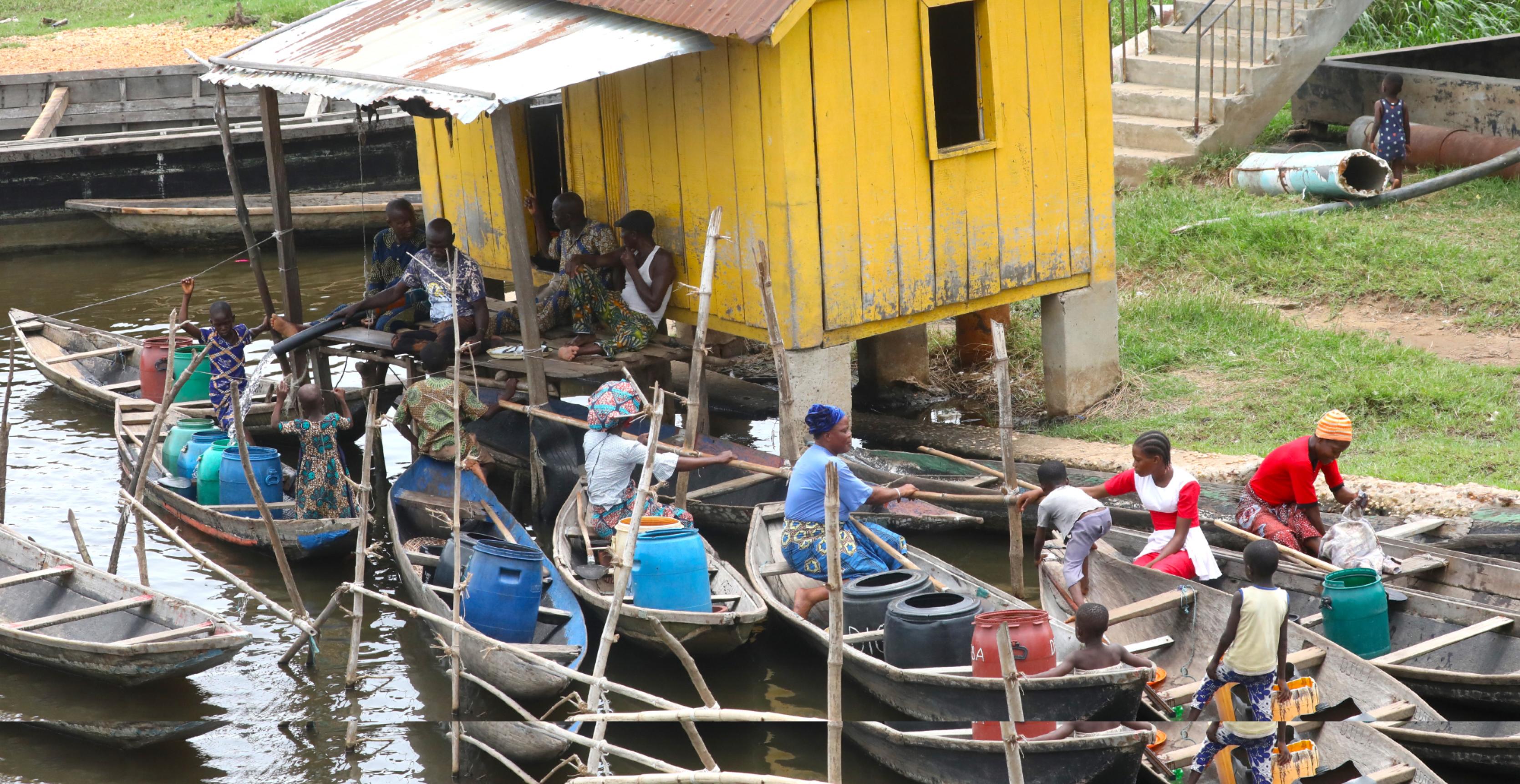 Viele Boote ankern vor einem Steg, von dem aus über einen dicken Schlauch Wasser in Kanister auf den Booten gepumpt wird.