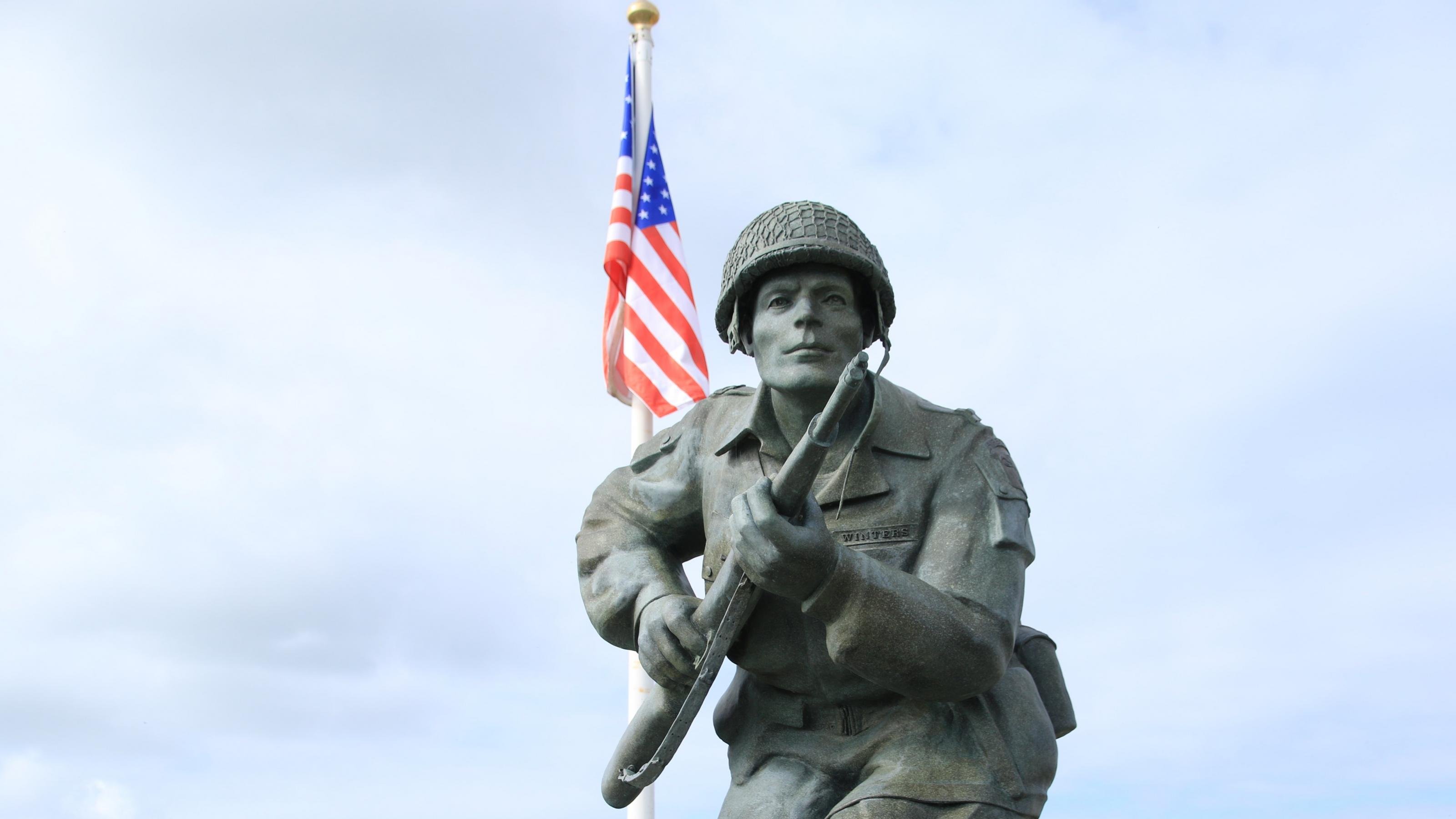 Eine Skulptur zeigt einen amerikanischen Soldaten mit Gewehr und Marschgepäck, im Hintergrund weht die US-amerikanische Fahne