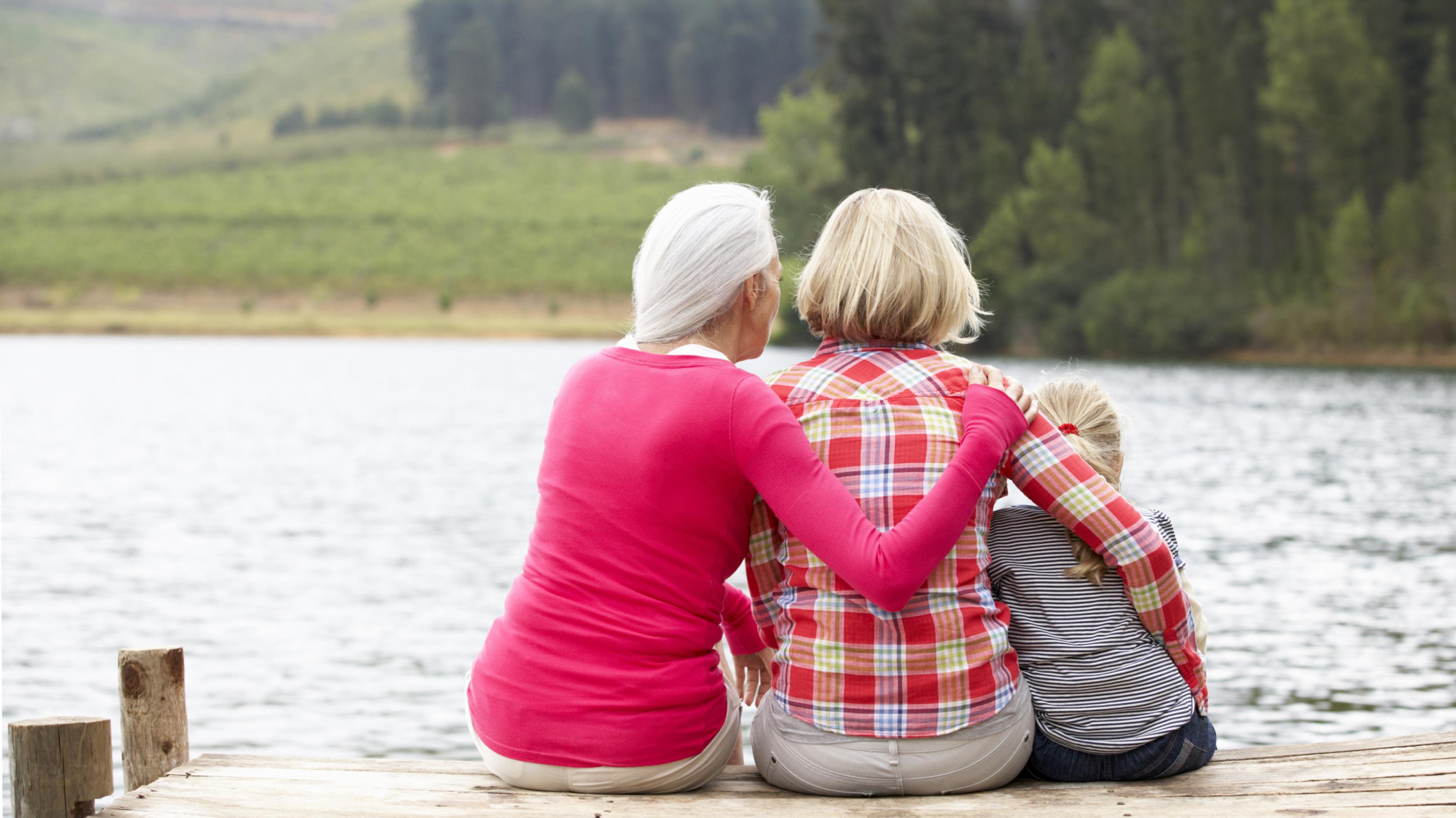 Großmutter, Mutter und Tochter sitzen auf einem Steg am See.