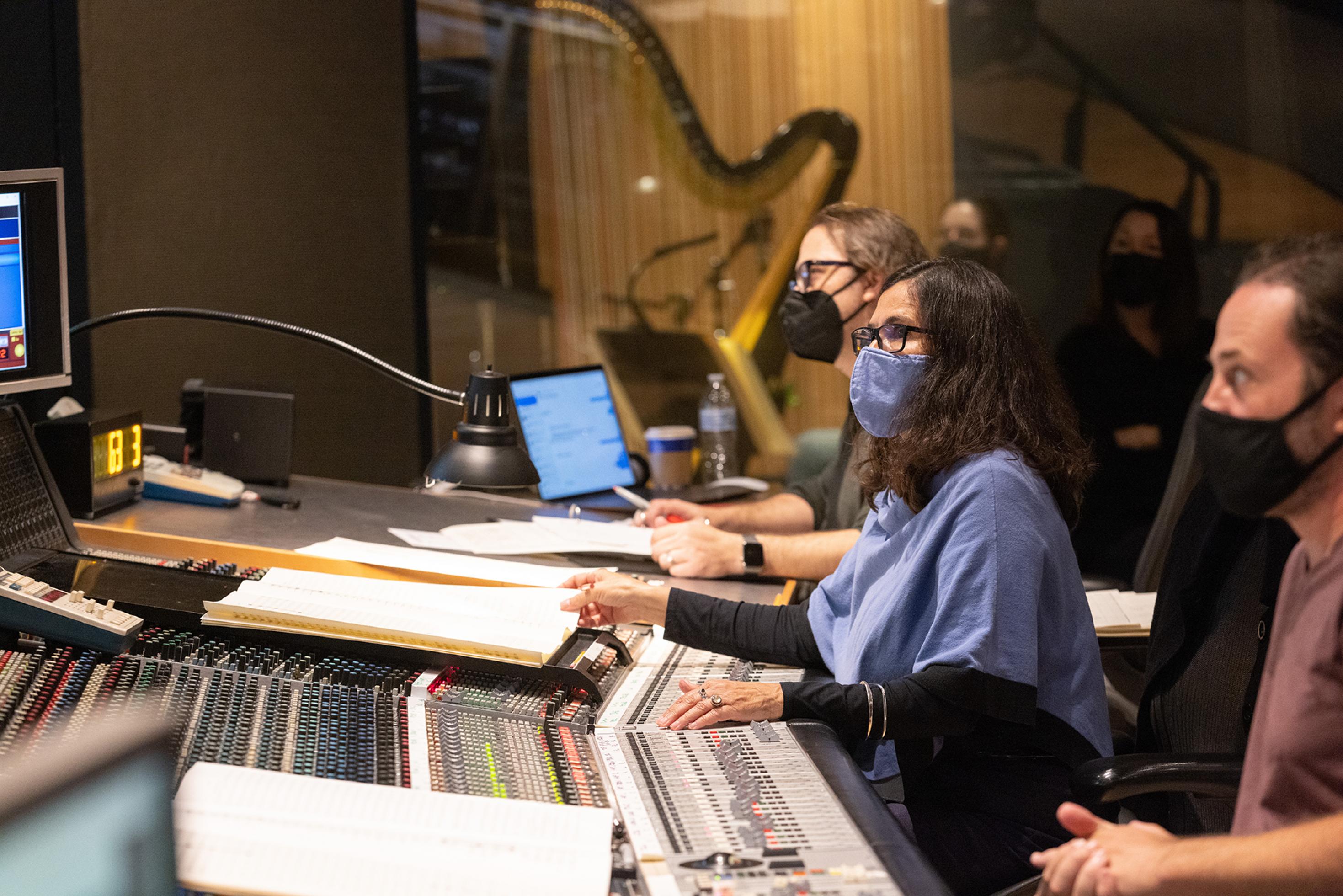 Komponistin Germaine Franco trägt bei der Arbeit im Disney Tonstudio wegen der Pandemie eine blaue Stoffmaske. An den Reglern und mit den Noten vor sich schaut sie konzentriert zu den Musikern, die nicht im Bild sind.