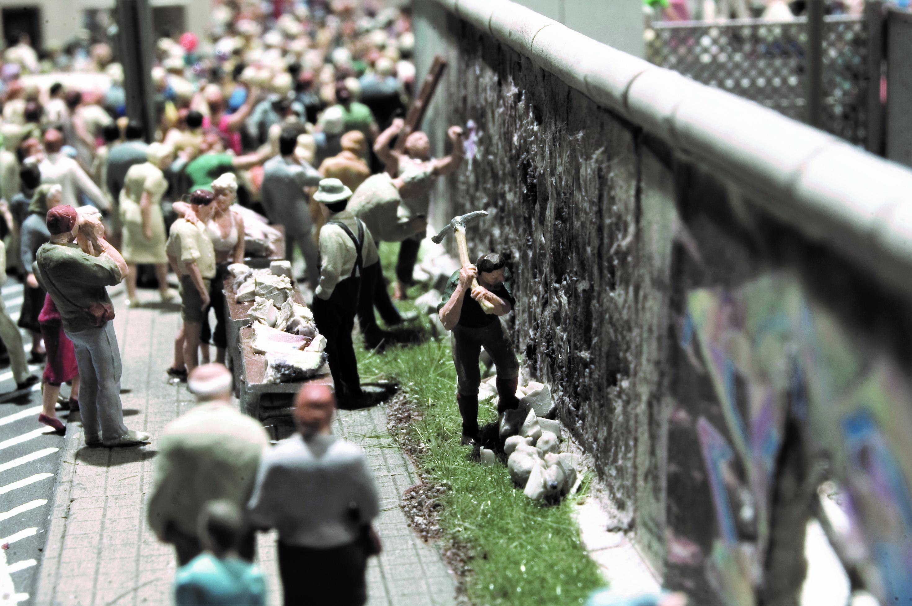 Ein Mann holt mit einer großen Spitzhacke gewaltig aus, um der Berliner Mauer ein weiteres Loch zuzufügen.