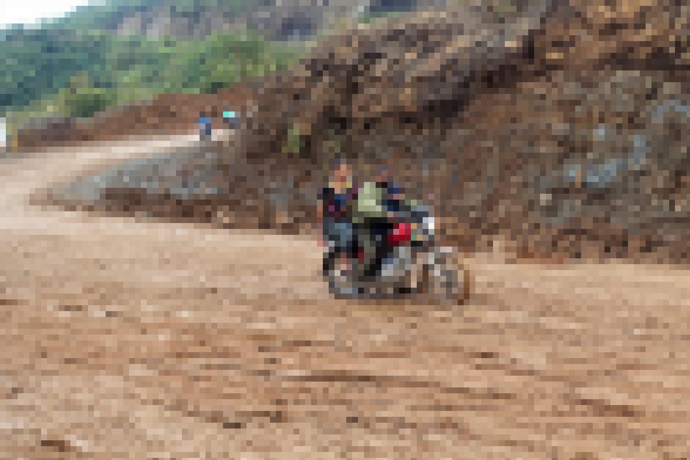 Zwei Menschen fahren auf einem Motorrad auf der schlammigen Straße zum Bergwerk der Firma CGN