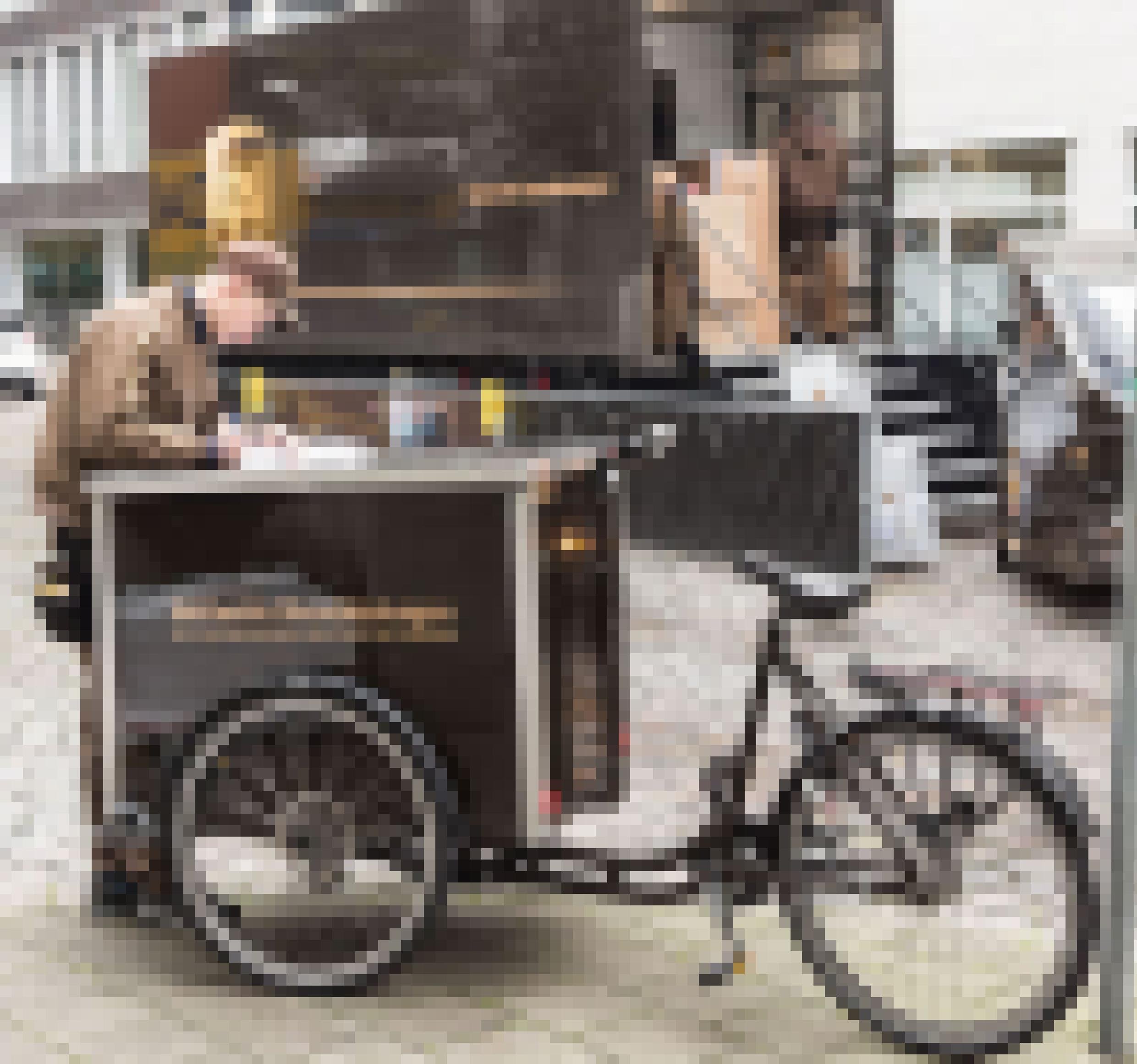 Ein Mann in brauner Arbeitskleidung steht hinter einem Lastenrad. Hinter ihm ist ein beladener LKW von UPS zu sehen.