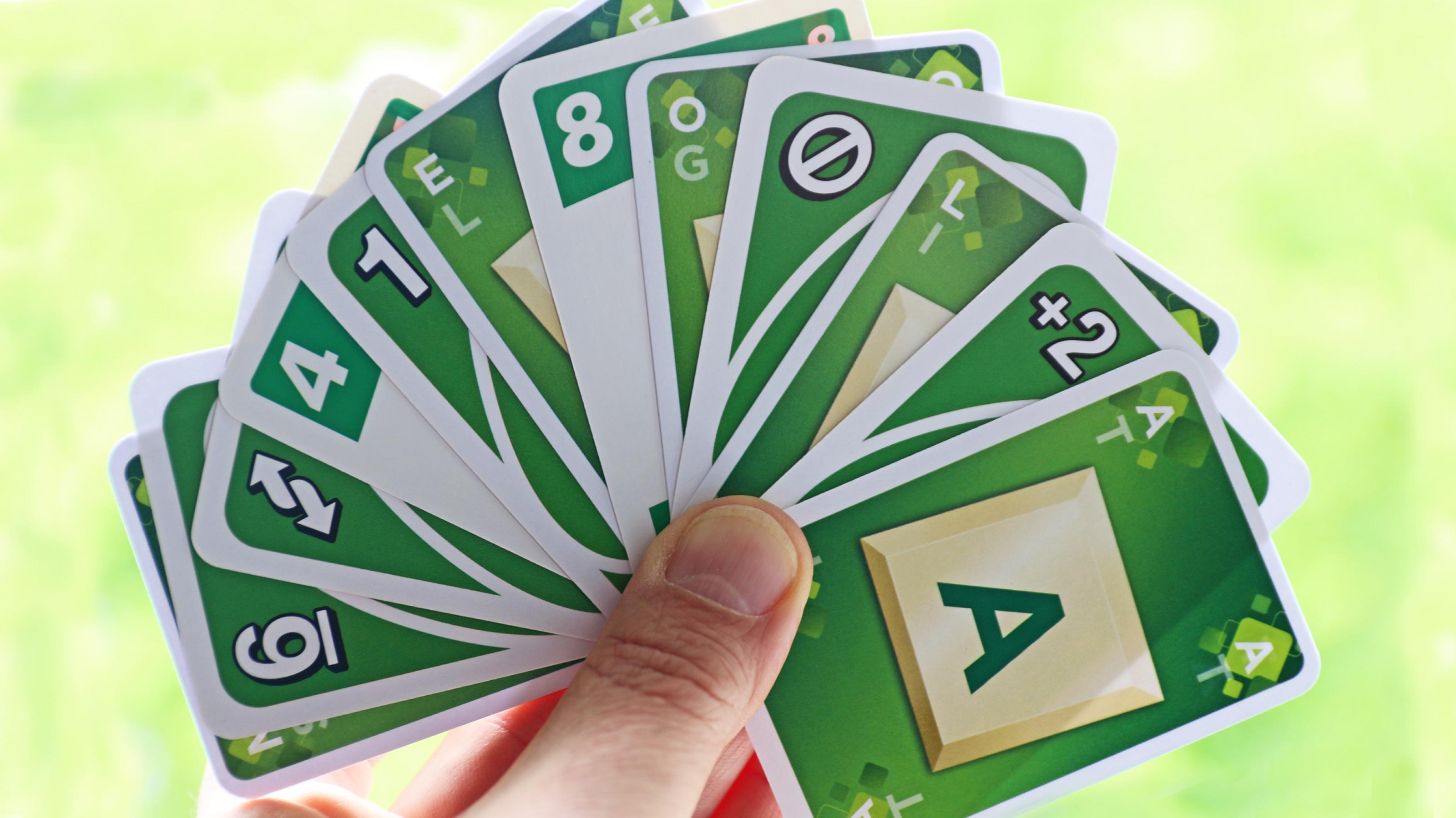 Eine Hand voller grüner Karten, die Buchstaben, Zahlen oder Anweisungen wie „+2“ zeigen.