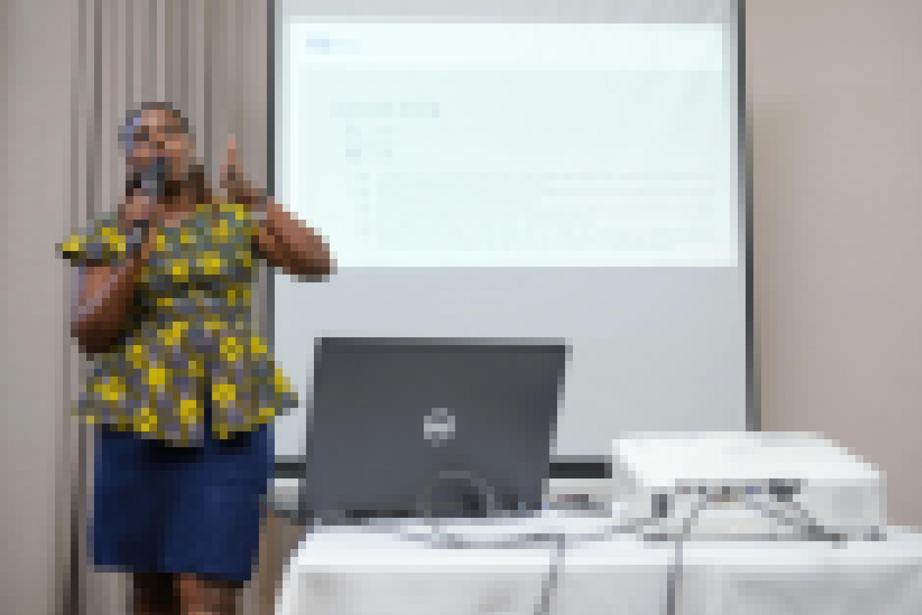 Das Foto zeigt Harriet Kamashanyu während eines Vortrages, bei dem sie einen Beamer einsetzt, sie steht vor einer Leinwand und spricht.