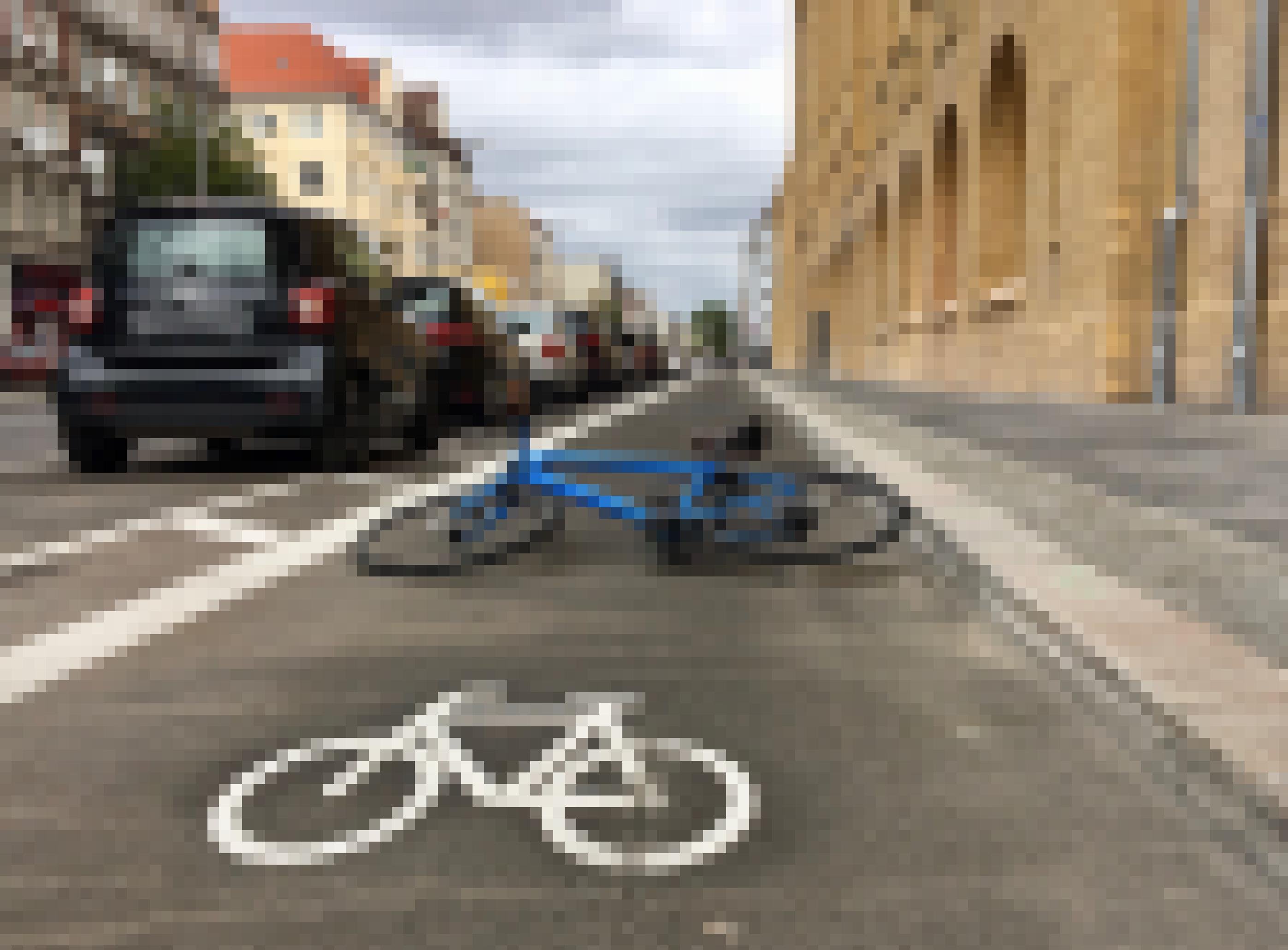 Eine Fahrradspur auf einer Straße mit parkendem Autos. Im Vordergrund ist das Piktogramm eines Fahrrades zu sehen, direkt dahinter liegt ein materielles, blaues Sportrad.
