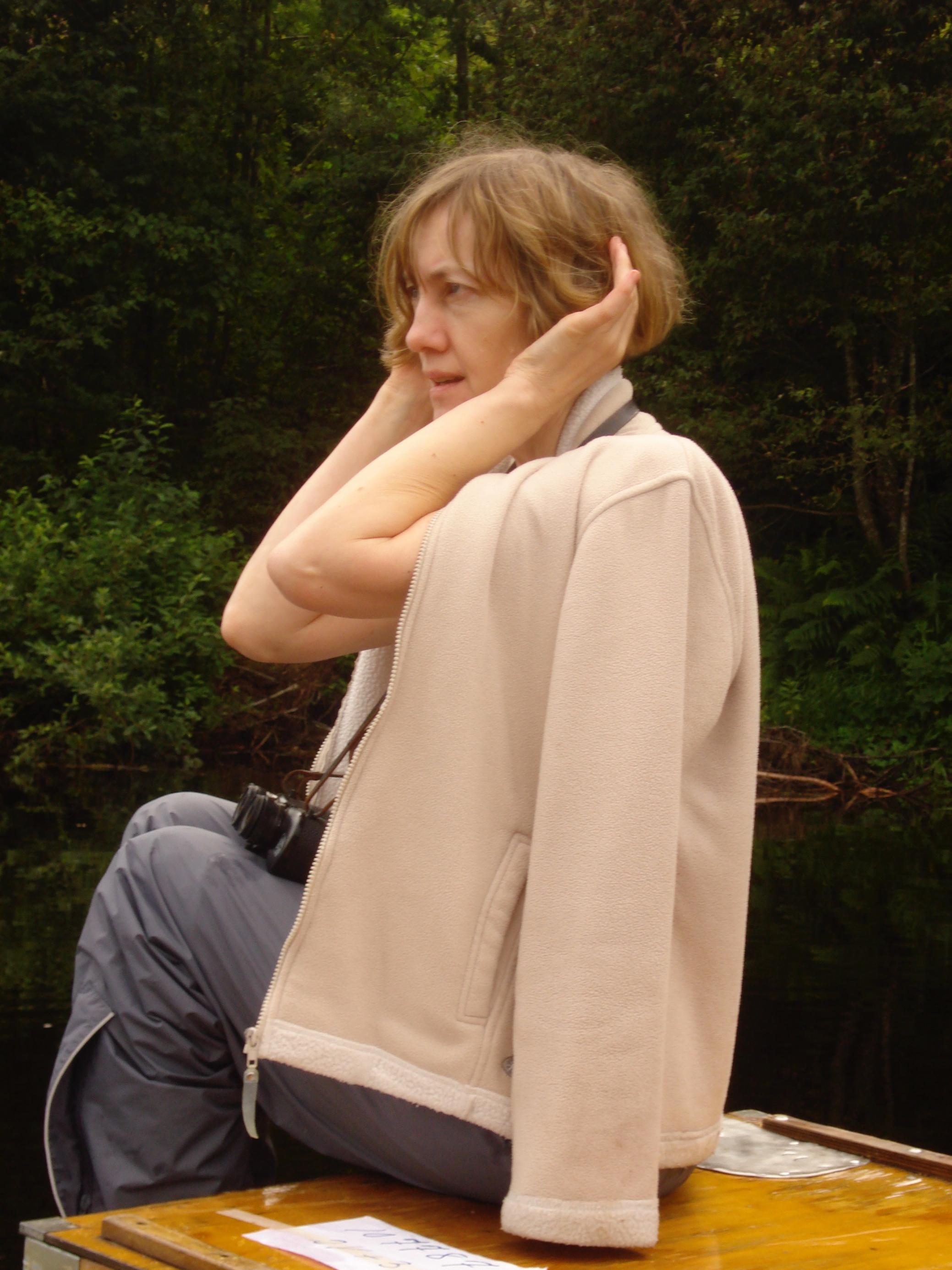 Flugbegleiterin Johanna Romberg hält sich beide Hände hinter die Ohren, um die Vogelstimmen in einem Wald zu idenfitizieren.