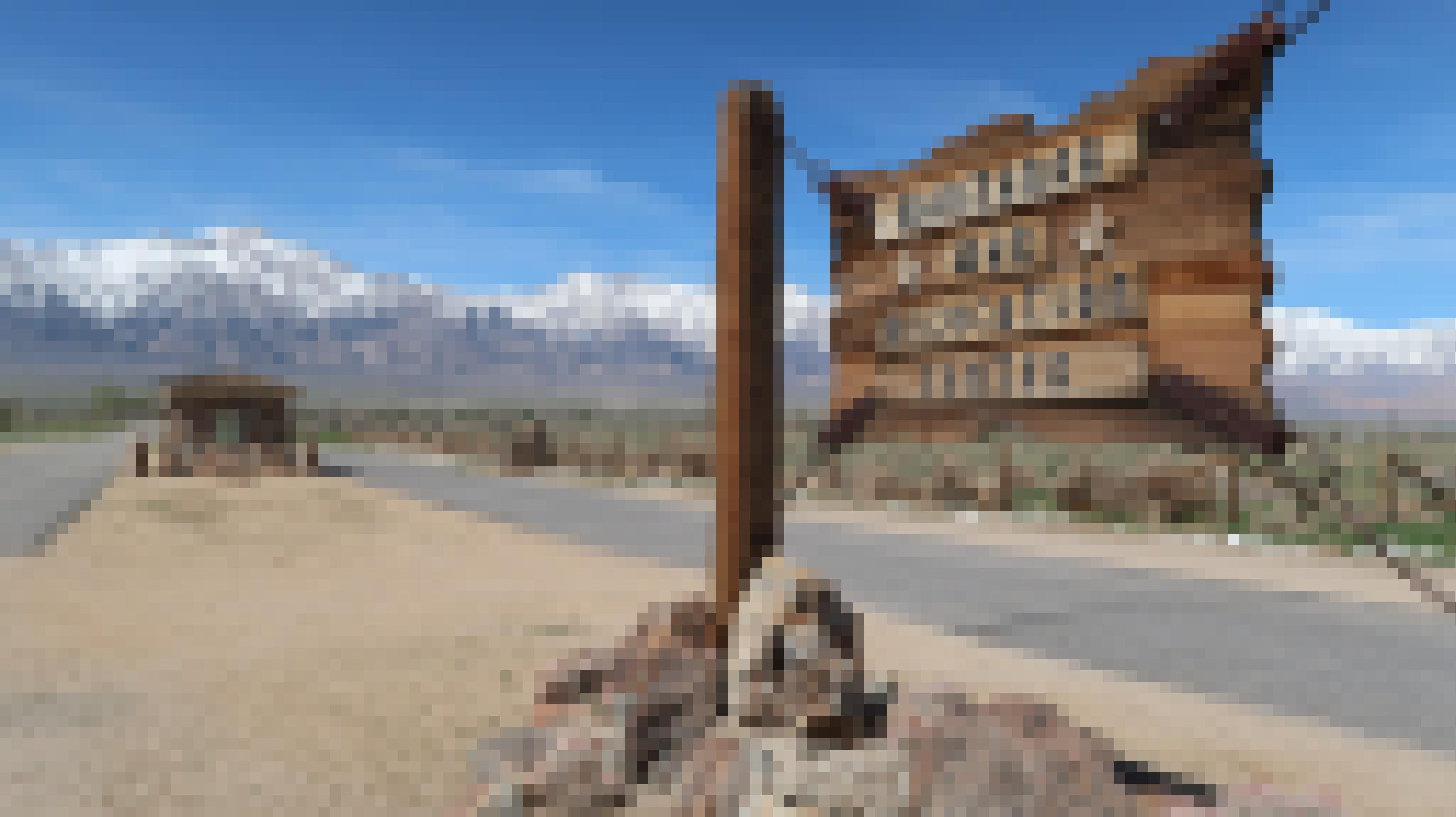Ein Holzschild mit der Aufschrift „Manzanar War Relocation Center“ vor blauem Himmel.