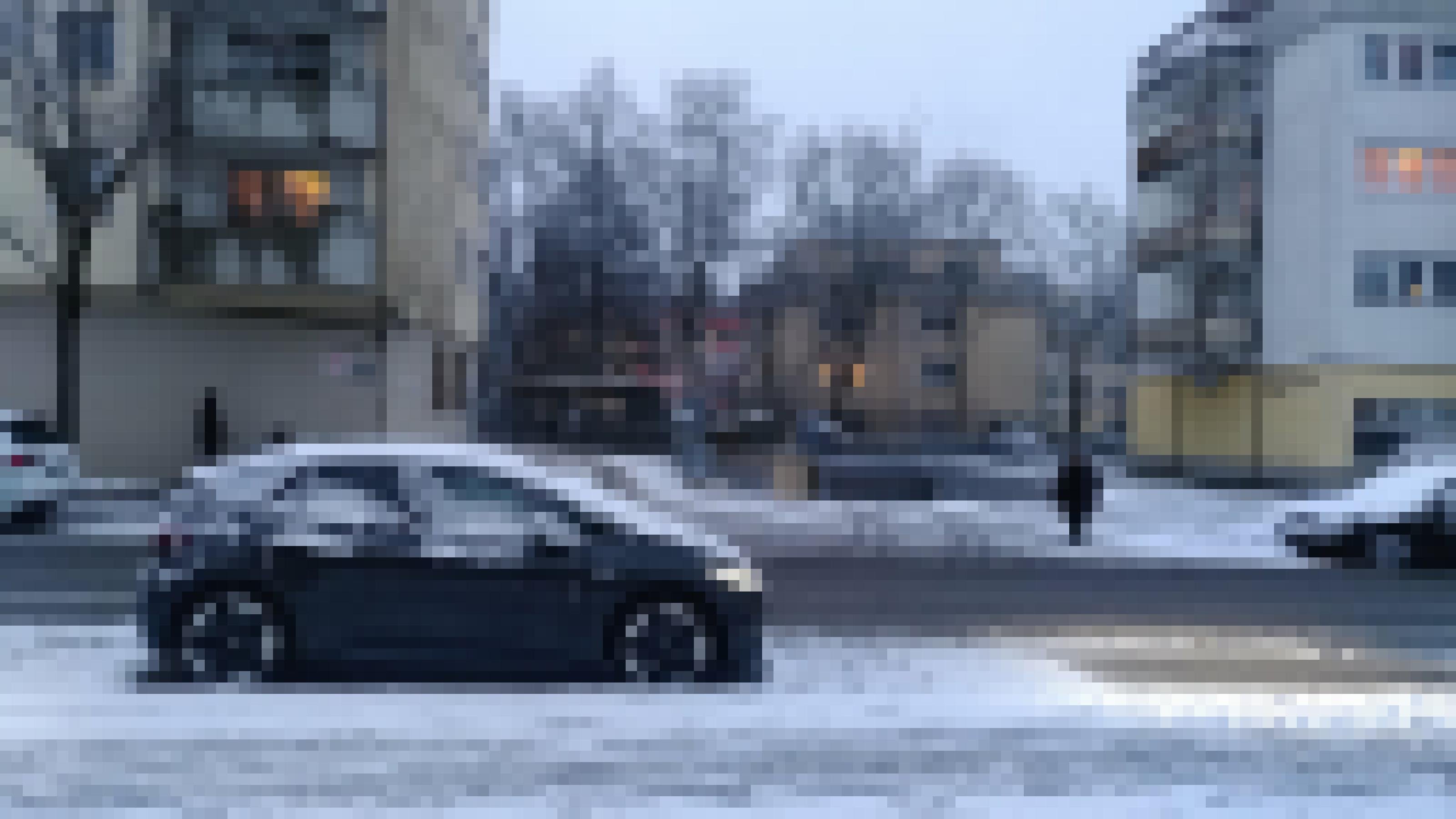Ein schneebedecktes Auto parkt am Straßenrand. Die Scheinwerfer sind an.
