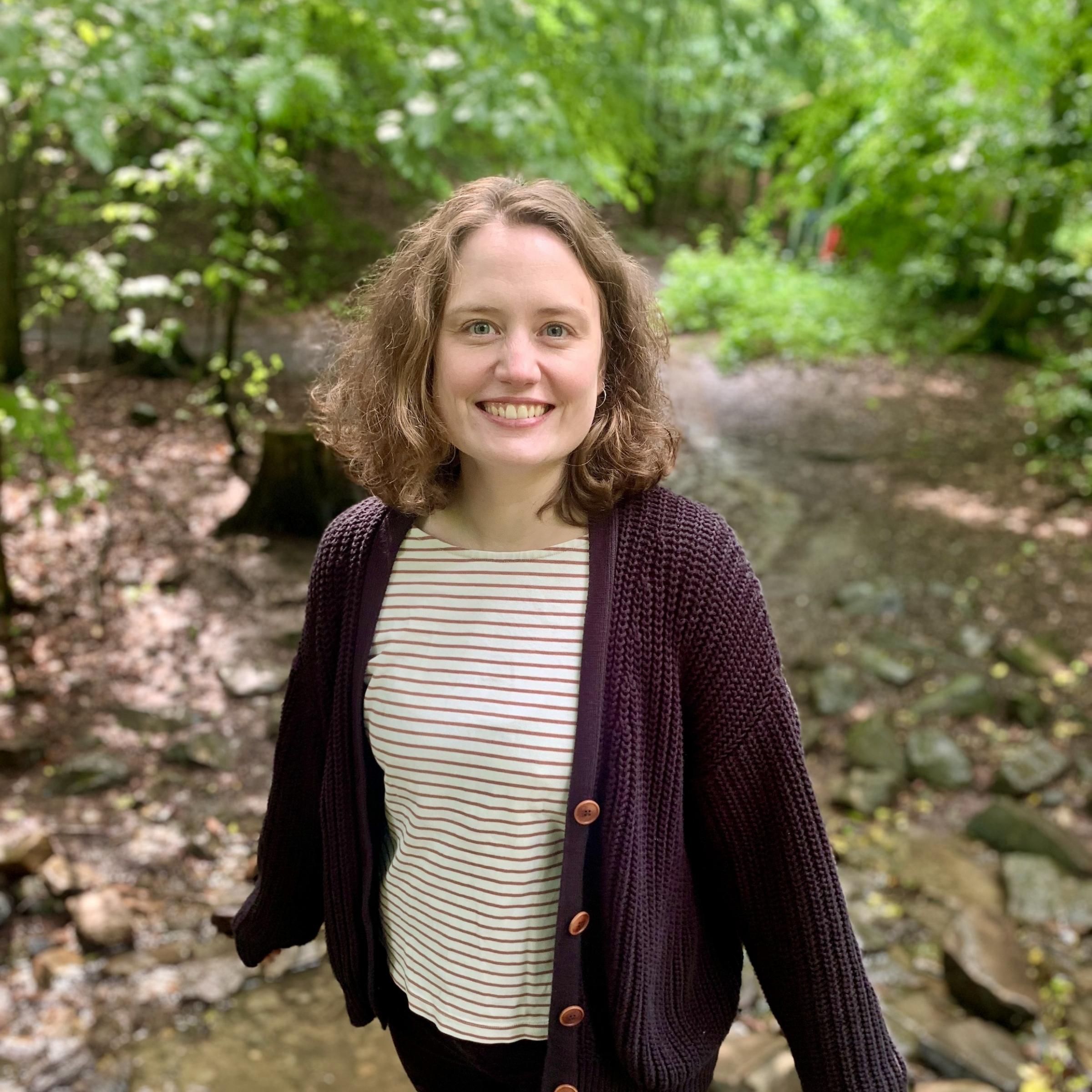 Eine Frau mit schulterlangen Haaren in einem geringelten Shirt schaut lächelnd in die Kamera.