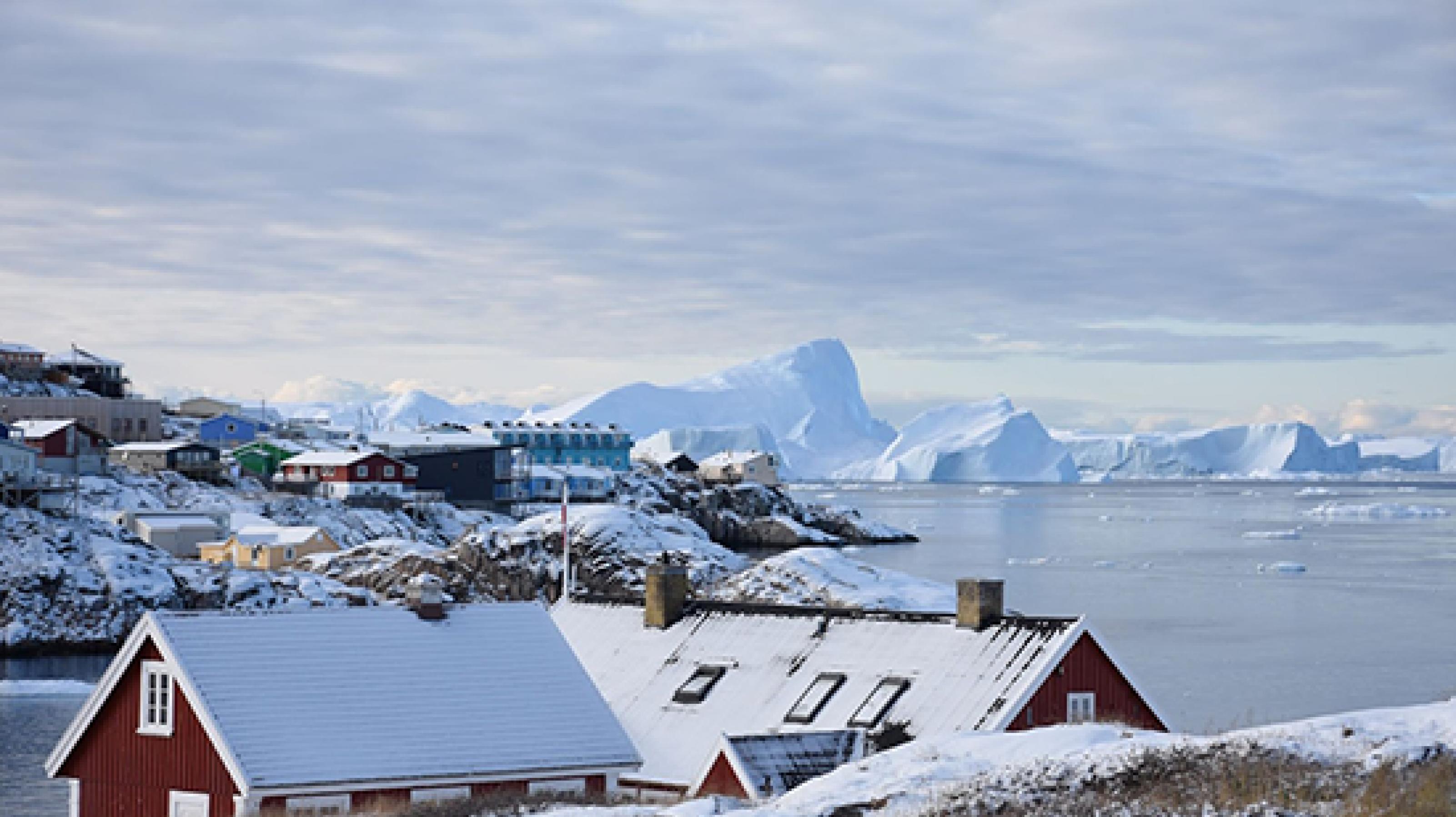Bunte Häuser im Vordergrund, im Hintergrund sind riesige Eisberge zu sehen
