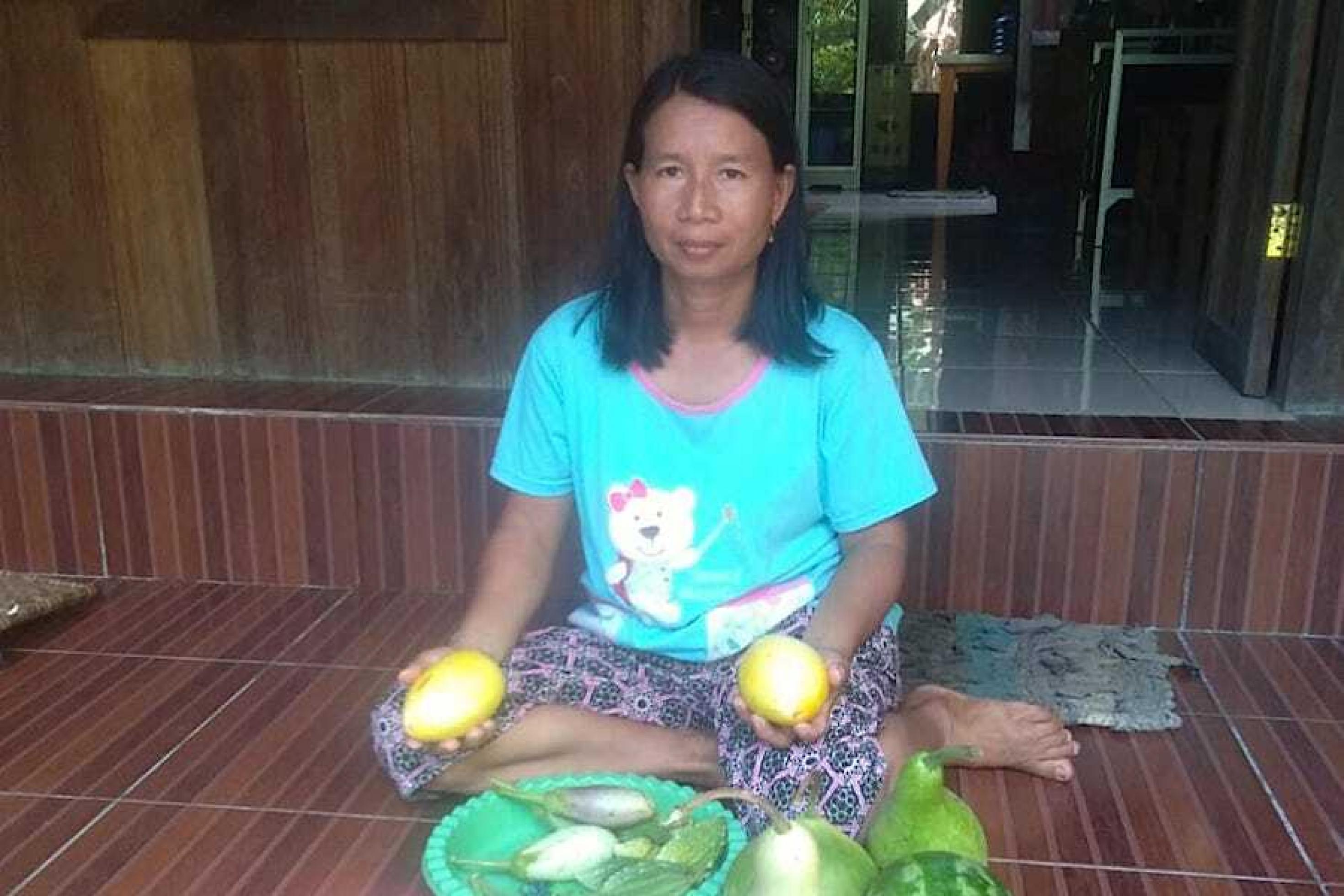 Die Bäuerin Mama Feri sitzt vor ihrem Hauseingang auf dem Boden und hat Auberginen, Bittergurken und Melonen aus eigenem Anbau vor sich liegen.