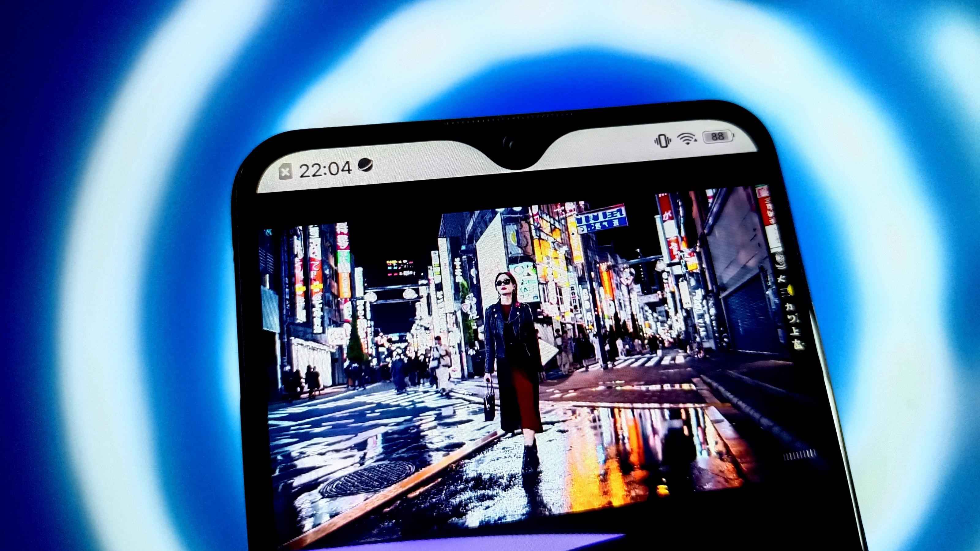 Ein Smartphone zeigt ein KI-generiertes Video einer stylish gekleideten Frau, die durchs nächtliche Tokio bummelt. Die Szene wirkt sehr realistisch.