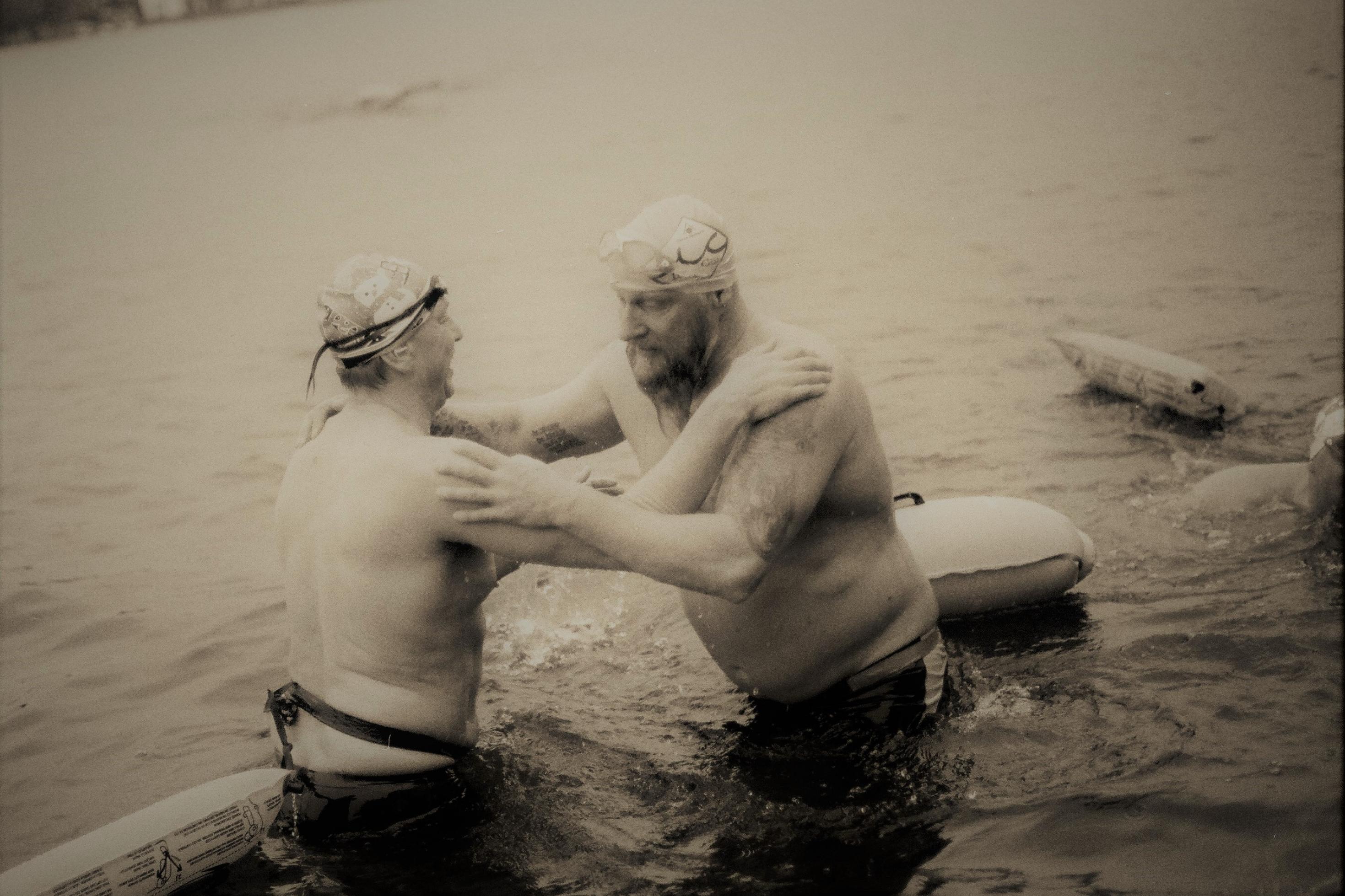 Zwei Männer nur in Badehose im eiskalten Wasser stehend.