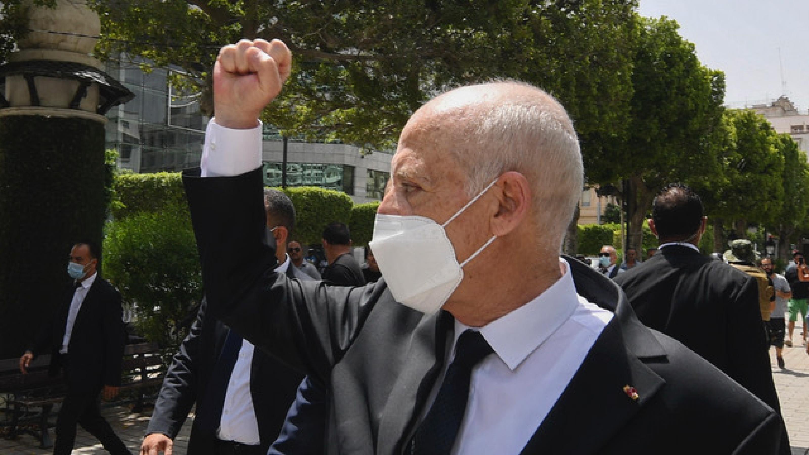 Tunesiens Präsident Kais Saïed geht über die Ave Bourguiba im Stadtzentrum der Hauptstadt Tunis. Er trägt einen schwarzen Anzug und eine FFP2-Maske. Die Hand hält er zur Faust geballt in die Höhe. Hinter und neben ihm laufen Personenschützer.