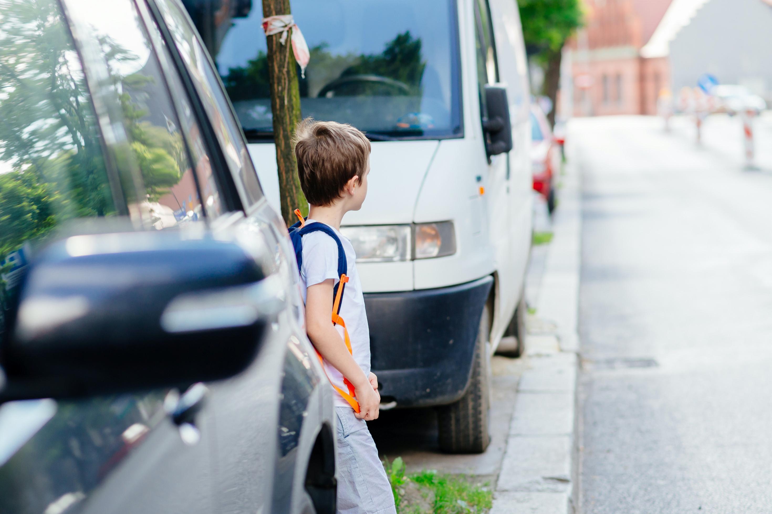 Little 7 years old boy during his road to school. He looks around to go to the other side of the street. Dressed in white t shirt and shorts
