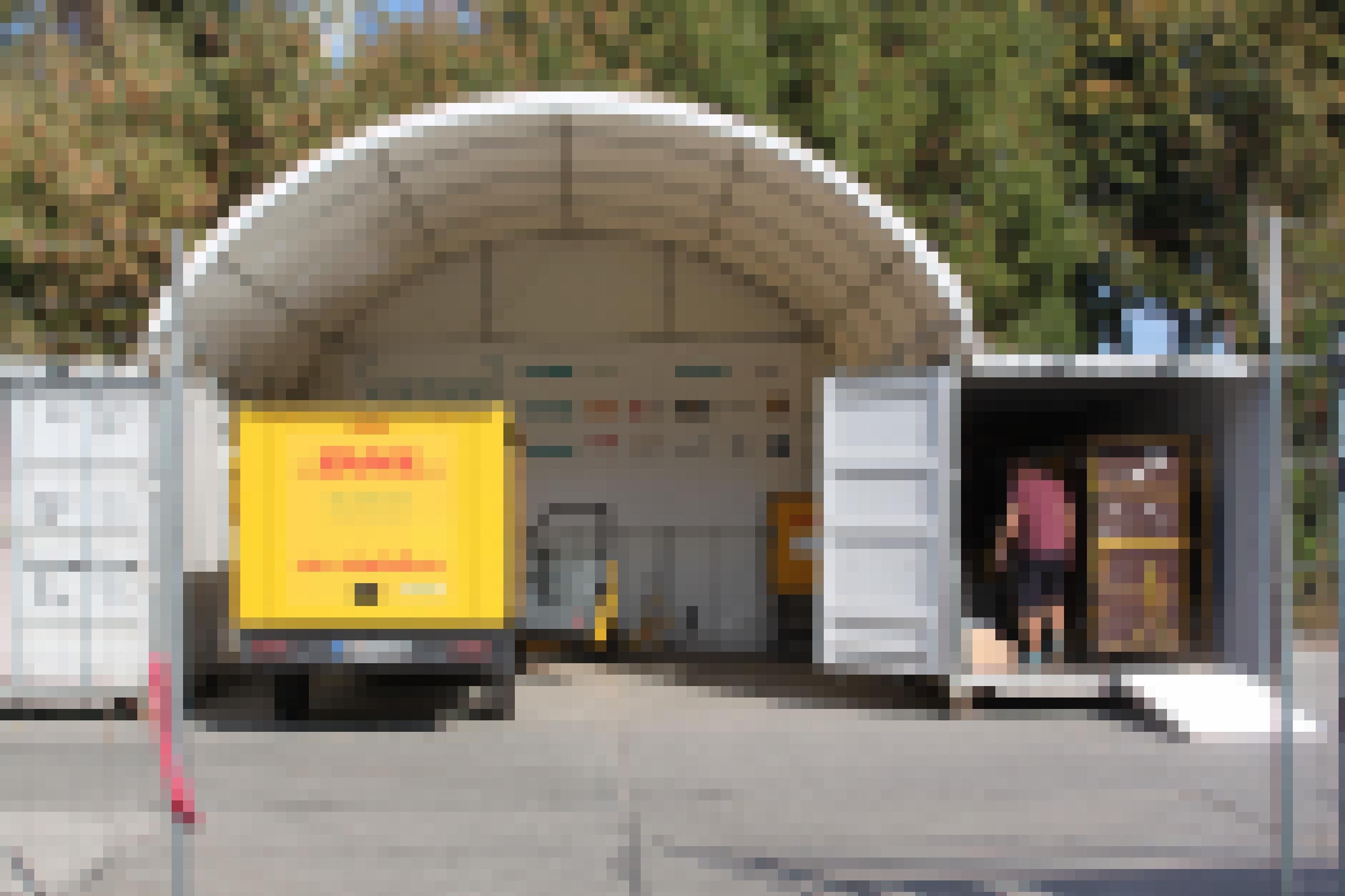 Ein kleiner DHL-Lastwagen steht unter einem runden Dach. Auf beiden Seiten sind Container zu sehen. Der rechte Container ist geöffnet, in ihm steht ein Mann.