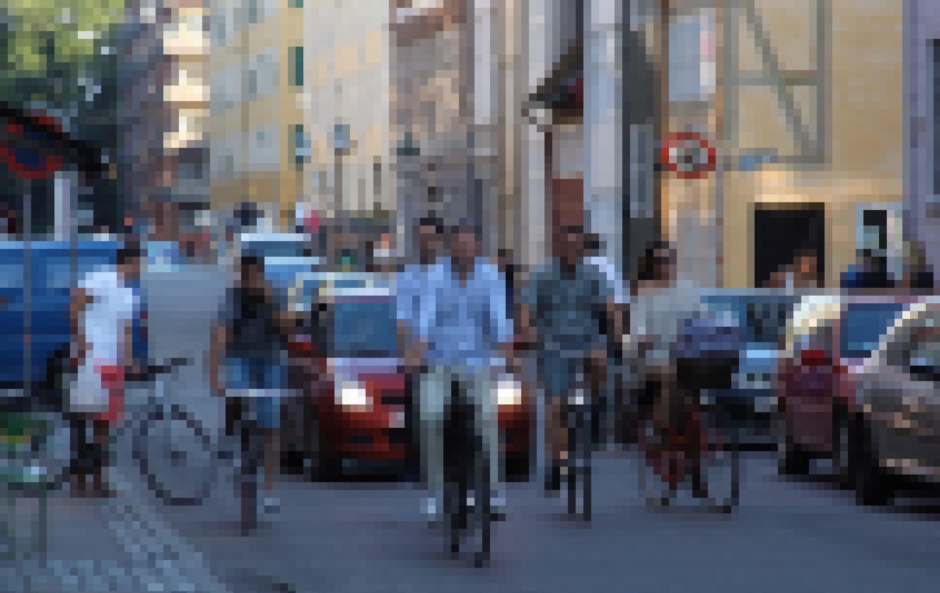 Auf einer kleinen Straße fahren viele Radfahrer. Hinter ihnen stauen sich einige Autos.