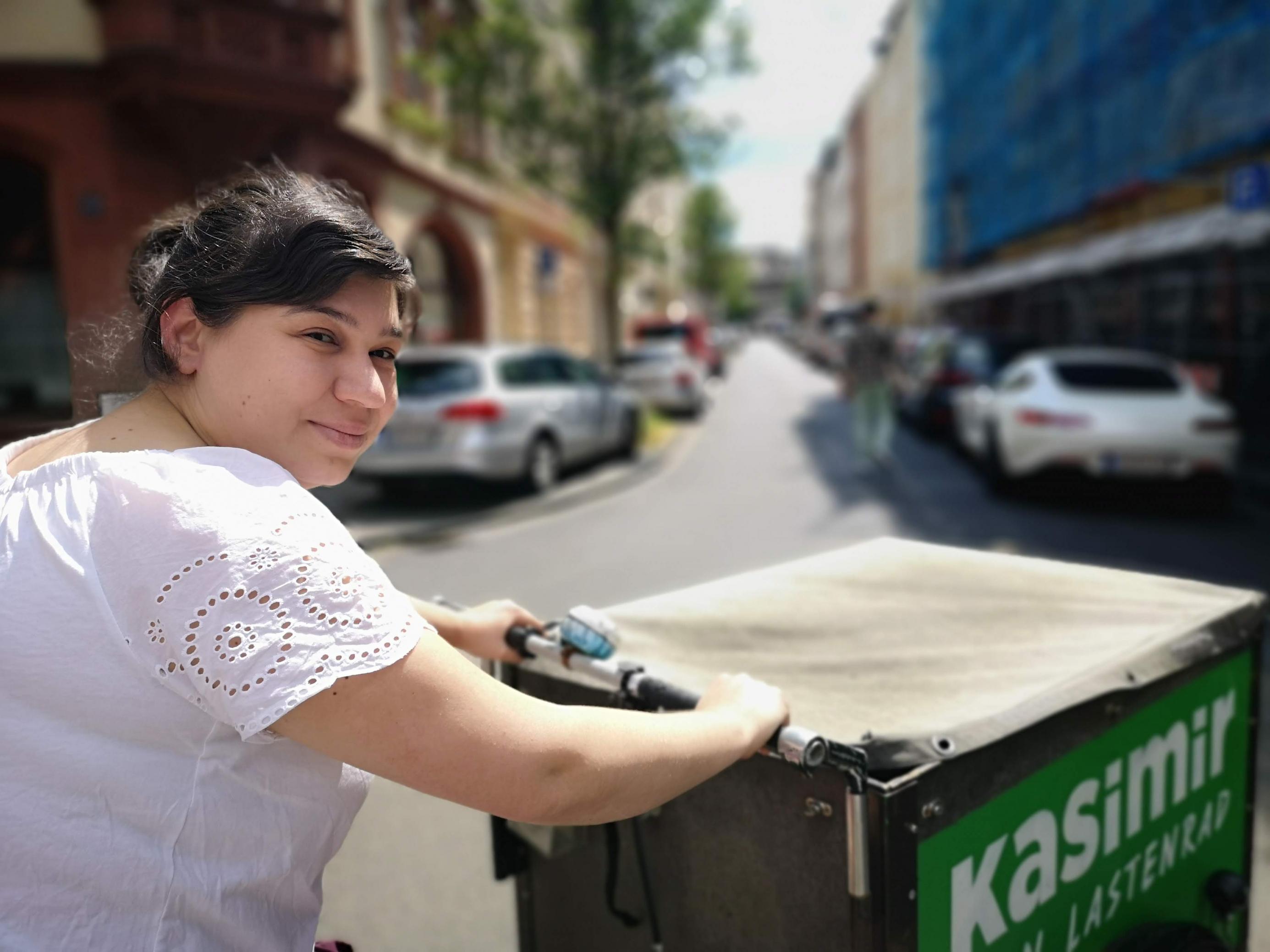 Fatma Erkus sitzt auf dem Lastenrad und blickt seitlich in die Kamera. Über ihre Schulter hinweg ist die große Box des Lastenrads von oben erkennbar. Sie wird mit einer Persenning gegen Regen geschützt