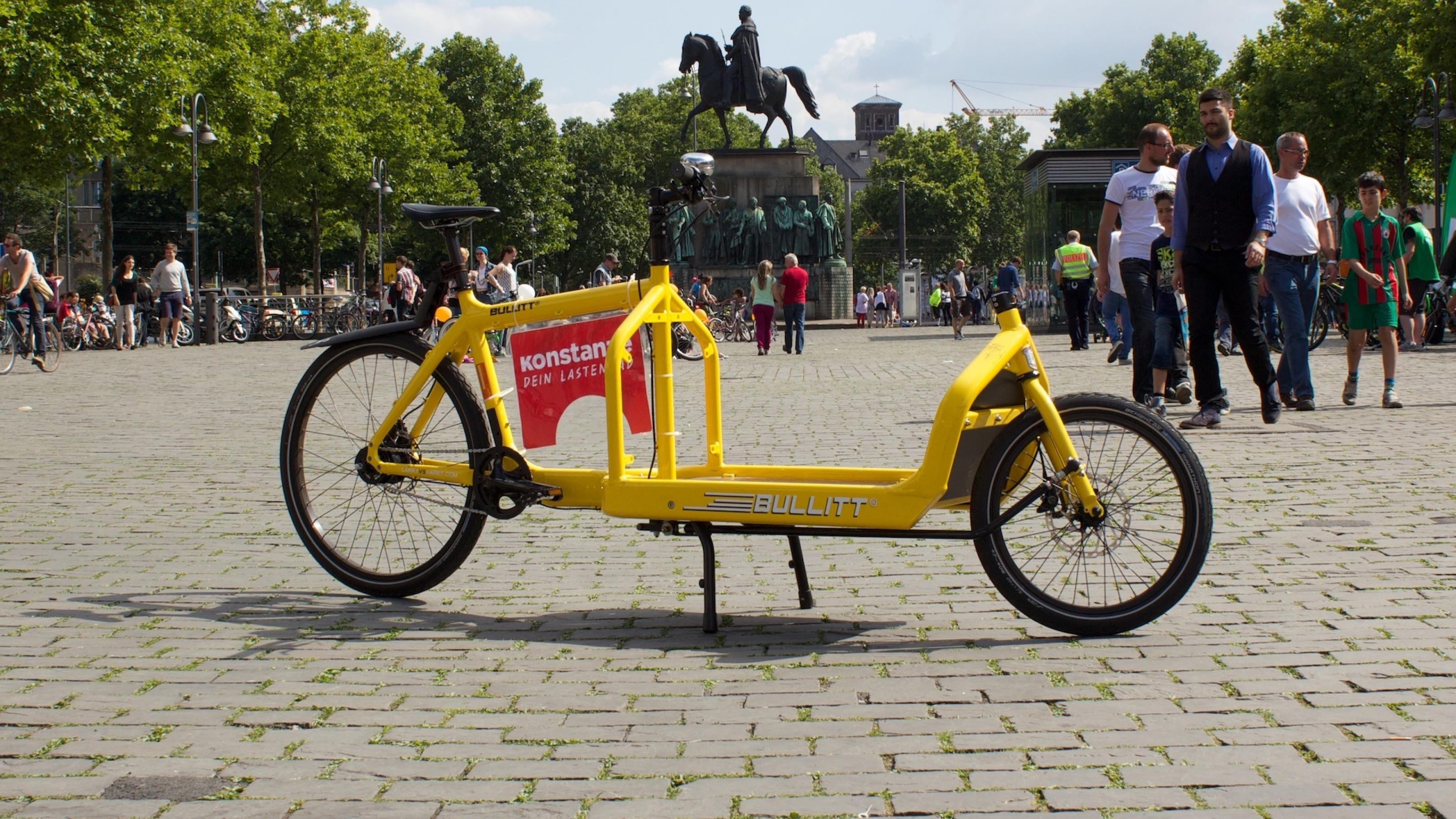 Das gelbe Lastenrad hat nur zwei Räder und fährt sich wie ein herkömmliches Fahrrad. Die Last kann vor dem Lenker befestigt werden. Es hat keine Box.
