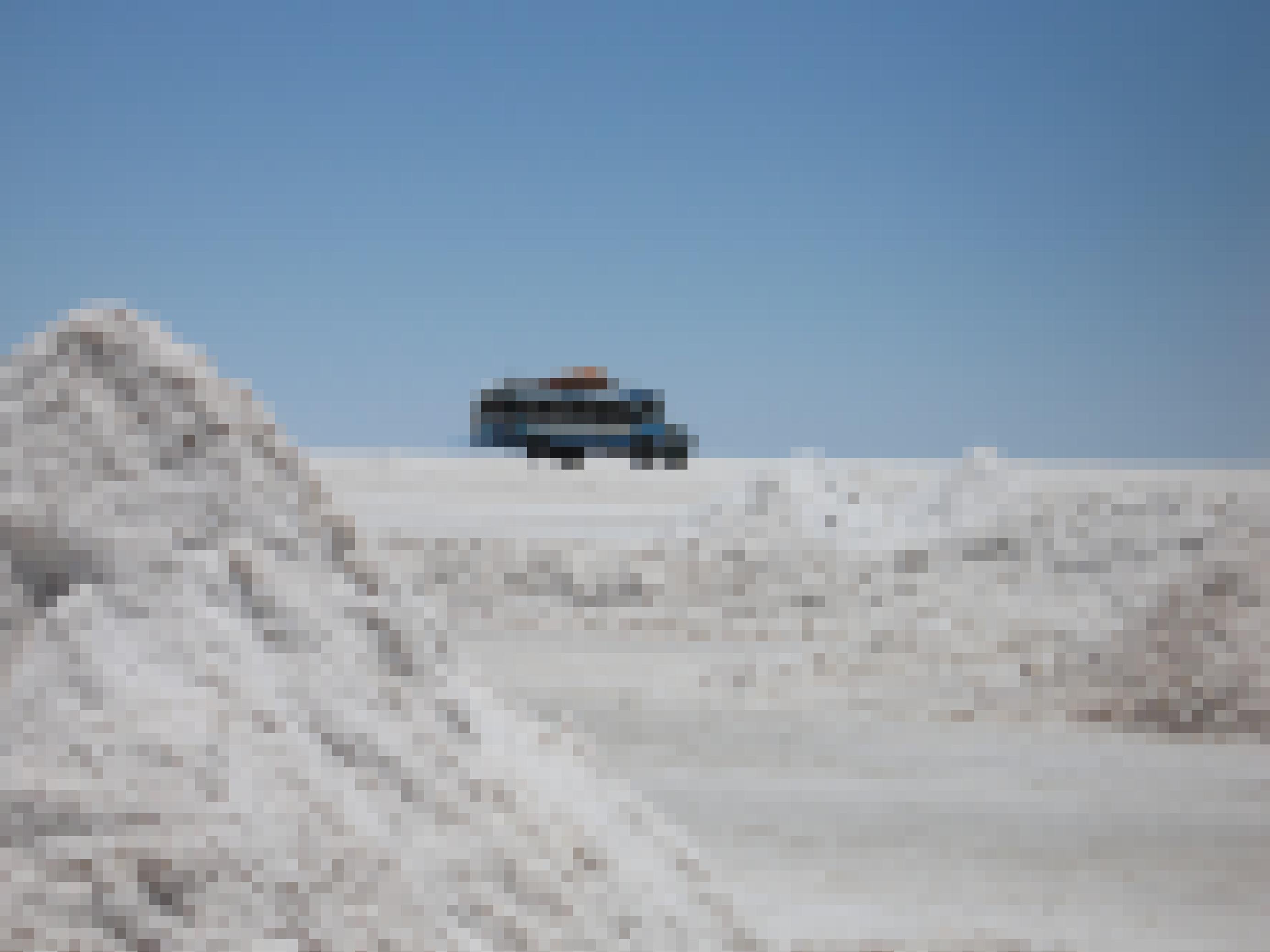 Eine weisse Salzwüste, ein dreieckiger Haufen, am Horizont fährt ein alter Bus vorbei.