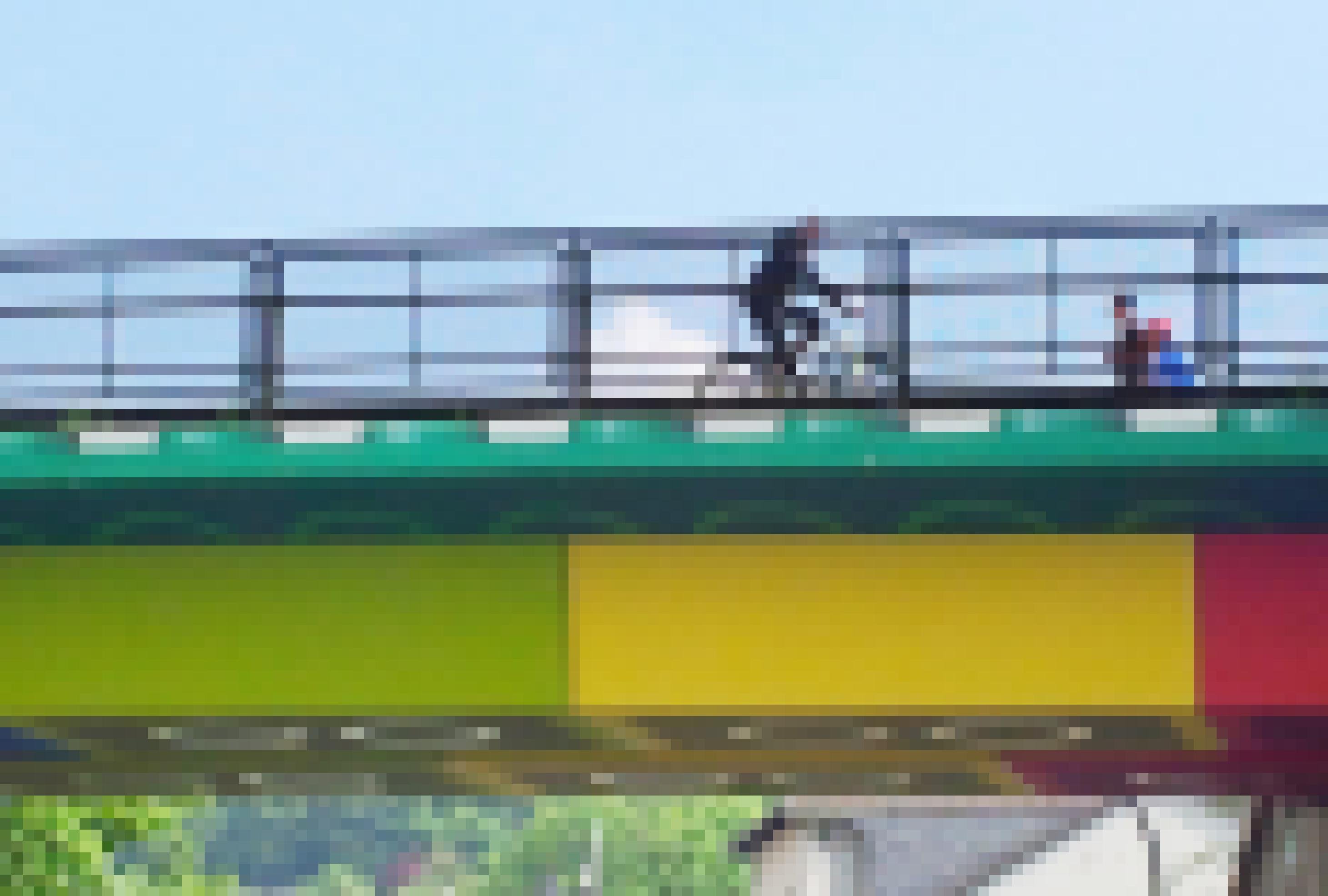 Ein Ausschnitt der Lego-Brücke, auf der ein Radfahrer und zwei Fußgänger hinter dem Geländer zu sehen sind. Der Himmel ist blau.