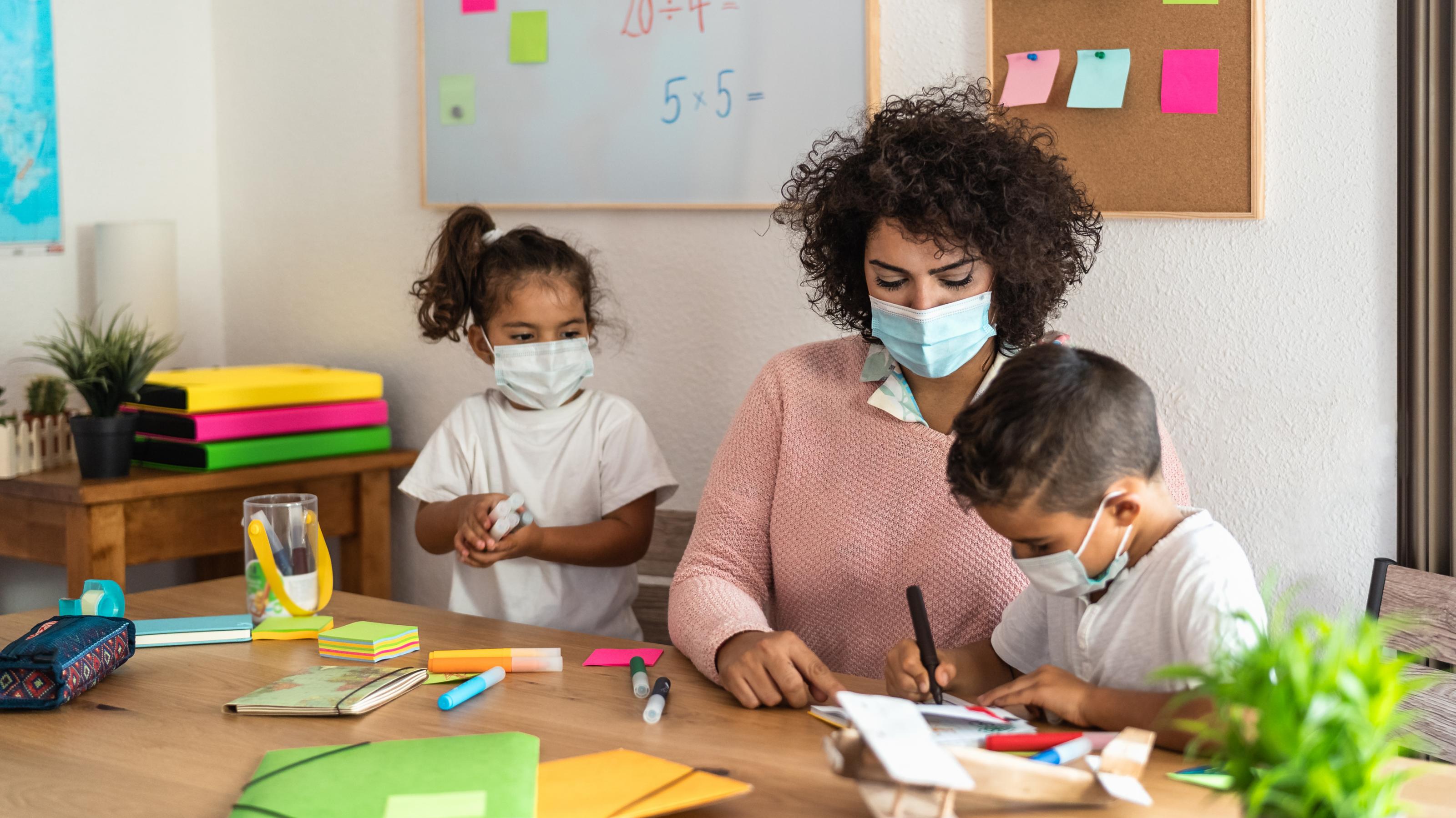 Eine Lehrerin mit Kindern in einem Klassenzimmer. Alle tragen Masken – denn diese sind ein effektiver Schutz vor dem Coronavirus.