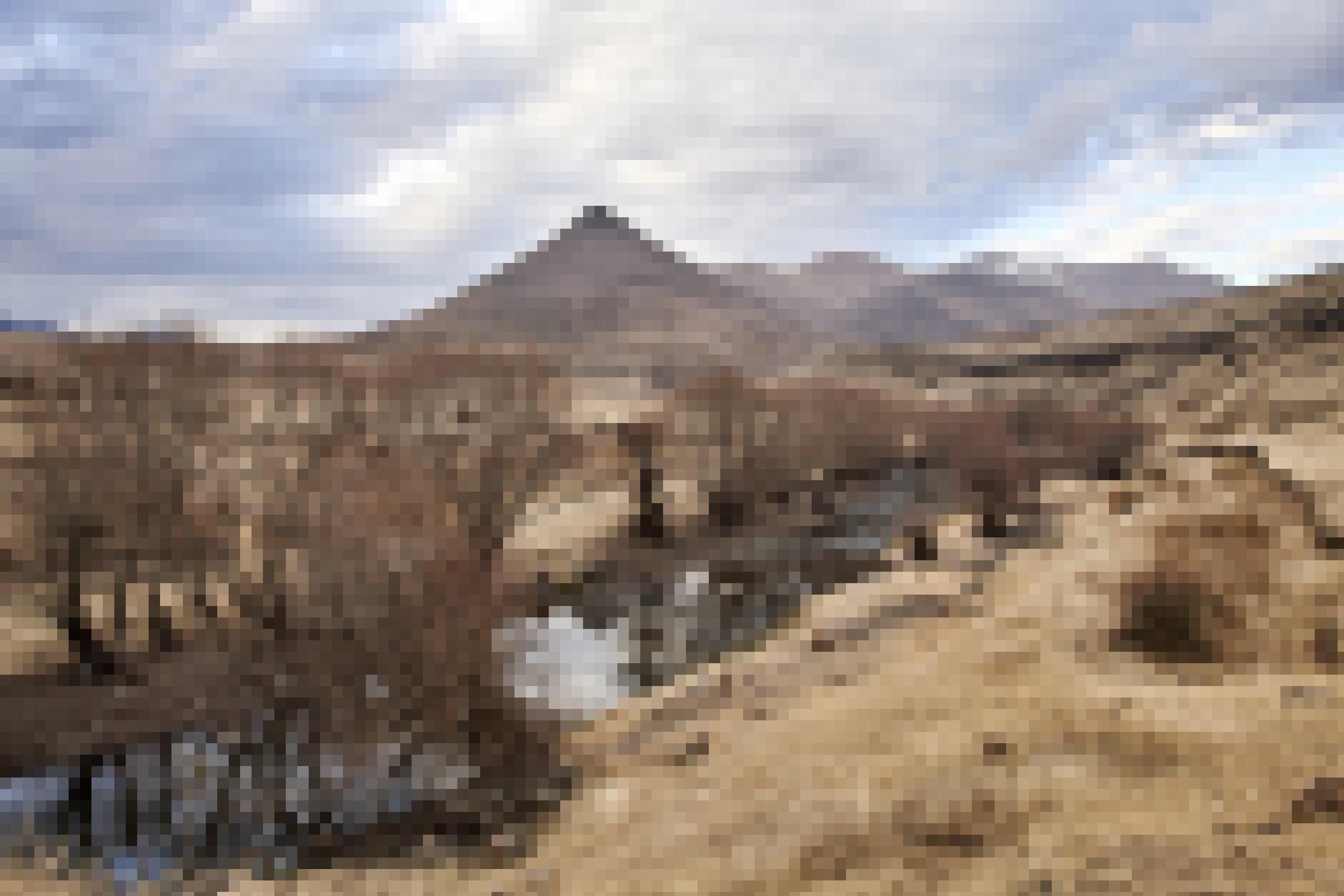 An dem Flussufer im Hochland Lesothos ist Erosion sichtbar, dahinter ragt ein pyramidenförmiger Berg in den Himmel