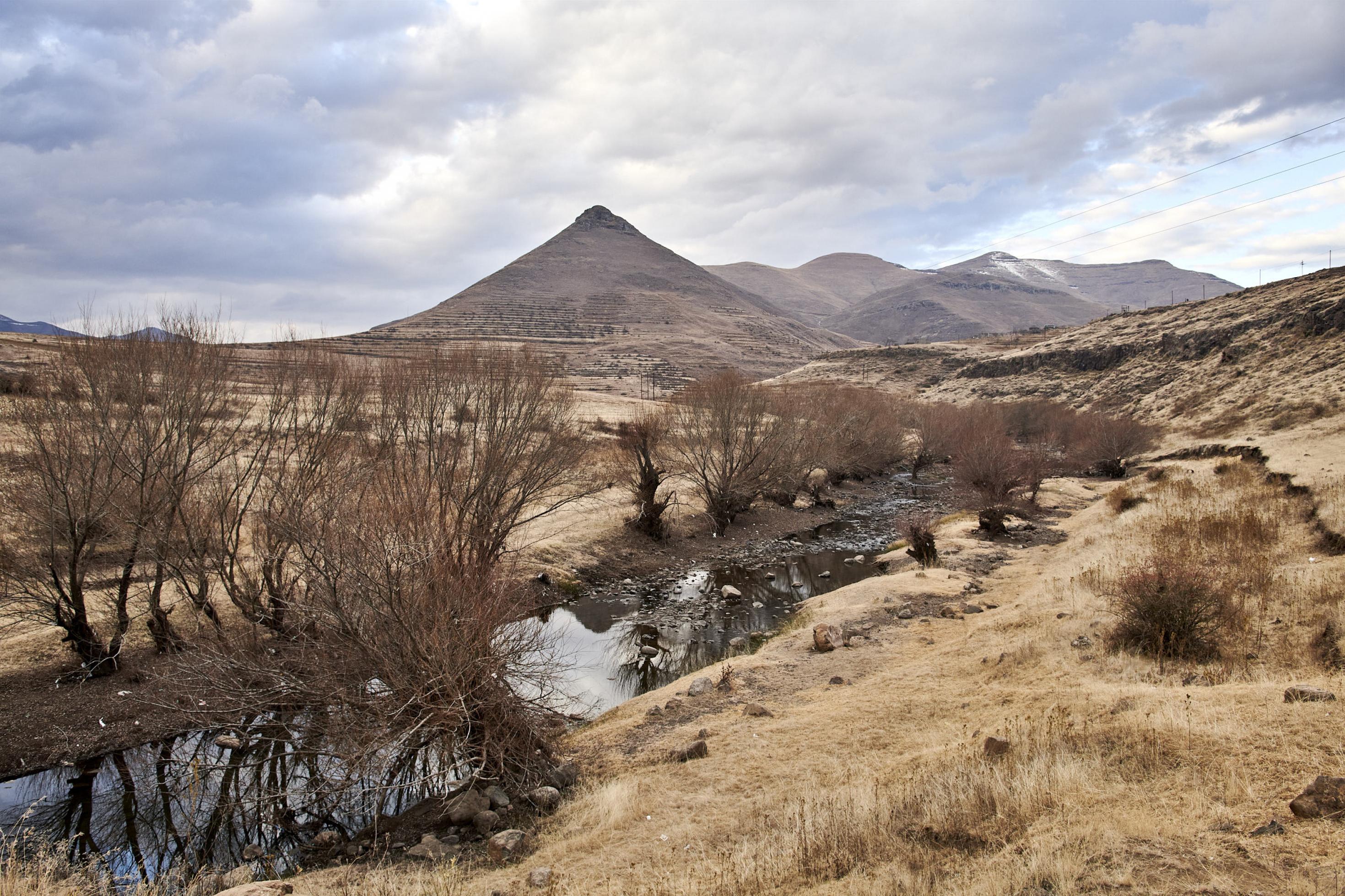 An dem Flussufer im Hochland Lesothos ist Erosion sichtbar, dahinter ragt ein pyramidenförmiger Berg in den Himmel