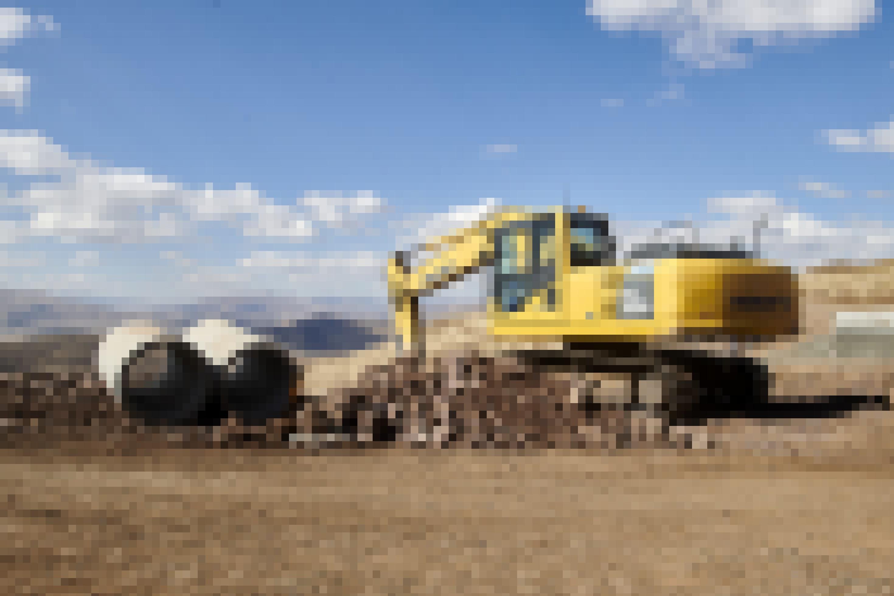 Ein gelber Bagger steht auf einem Steinhaufen, daneben liegen große Betonrohre