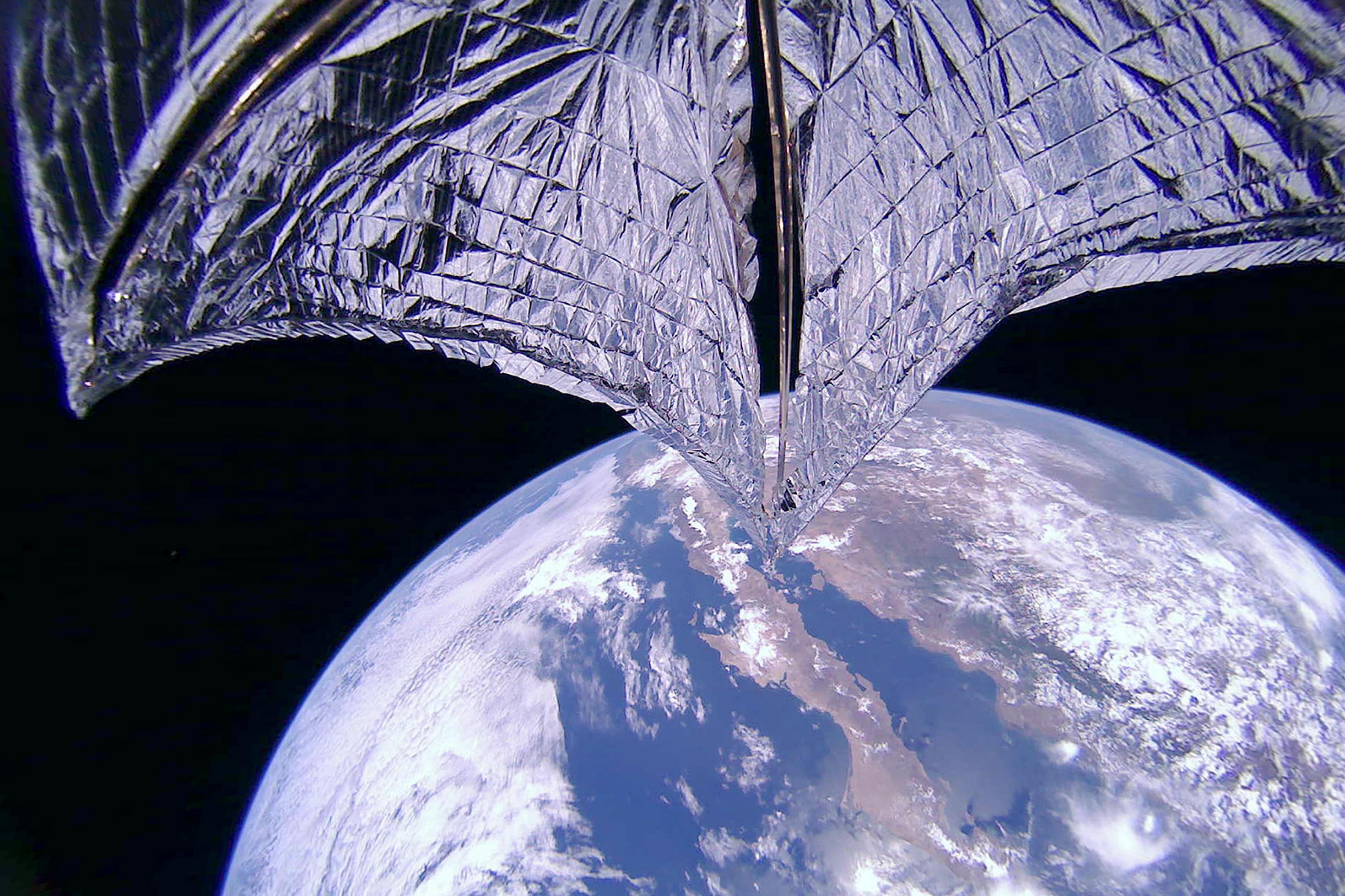 Eine Raumsonde im Erdorbit, angeschnitten ein Teil der silibrigen Segeloberfläche. Im Hintergrund schwarzer Himmel und ein Teil Kaliforniens.