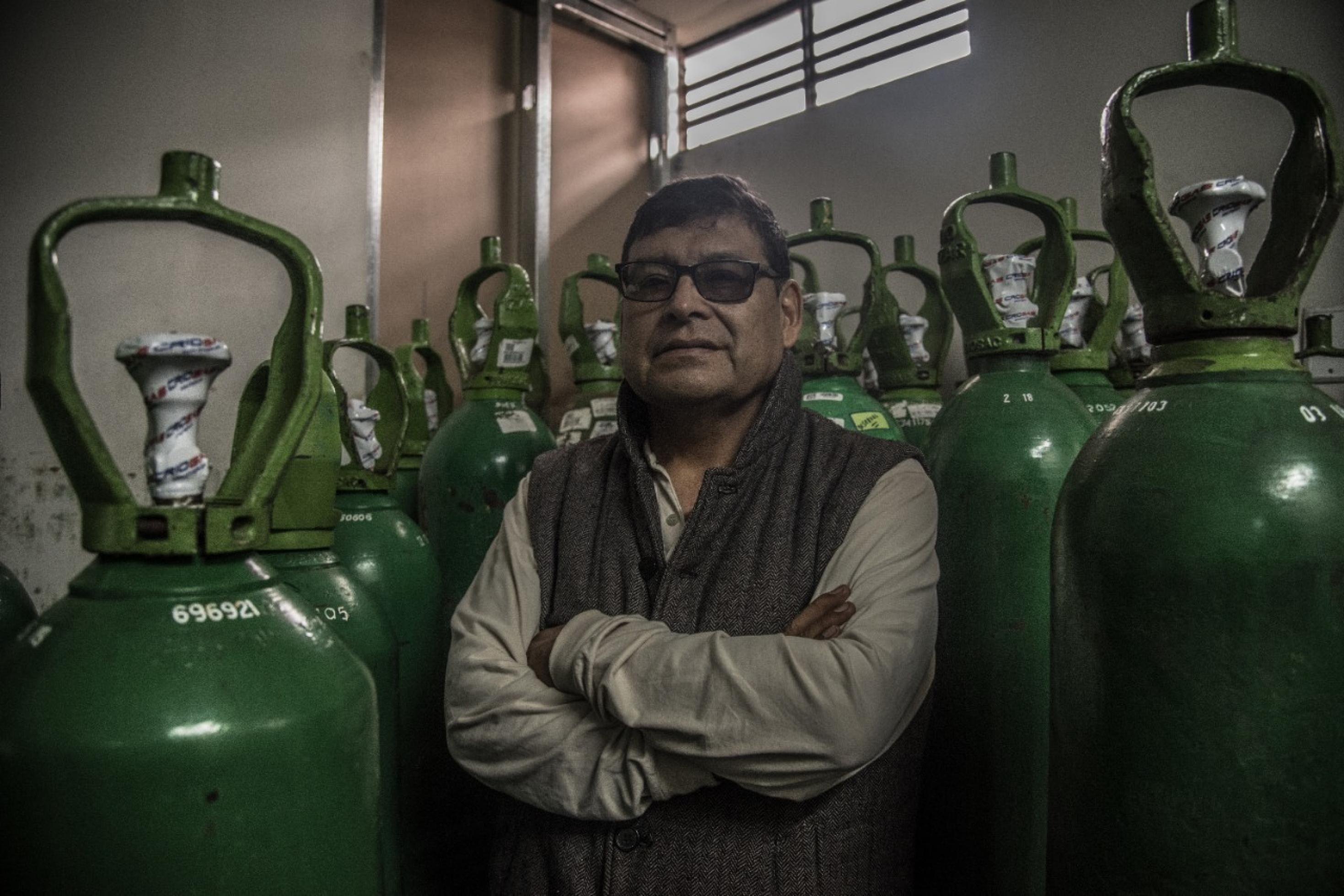 Rund 60-jähriger Mann mit Brille, verschränkten Armen, steht umgeben von grünen Sauerstoff-Flaschen aus Stahl.