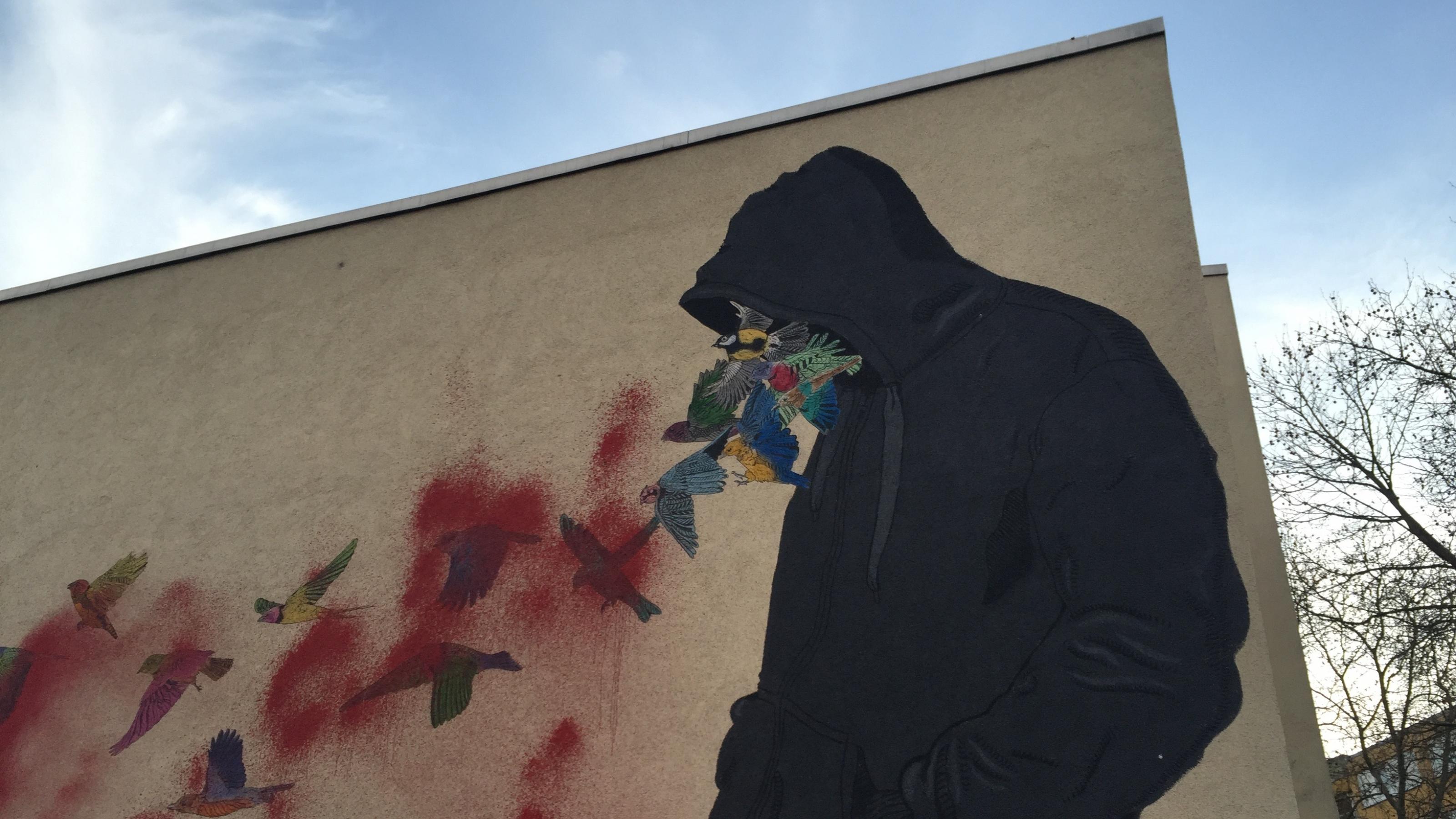 eine Wandmalerei eines Mannes mit einer Kapuze, aus der Vögel fliegen [AI]