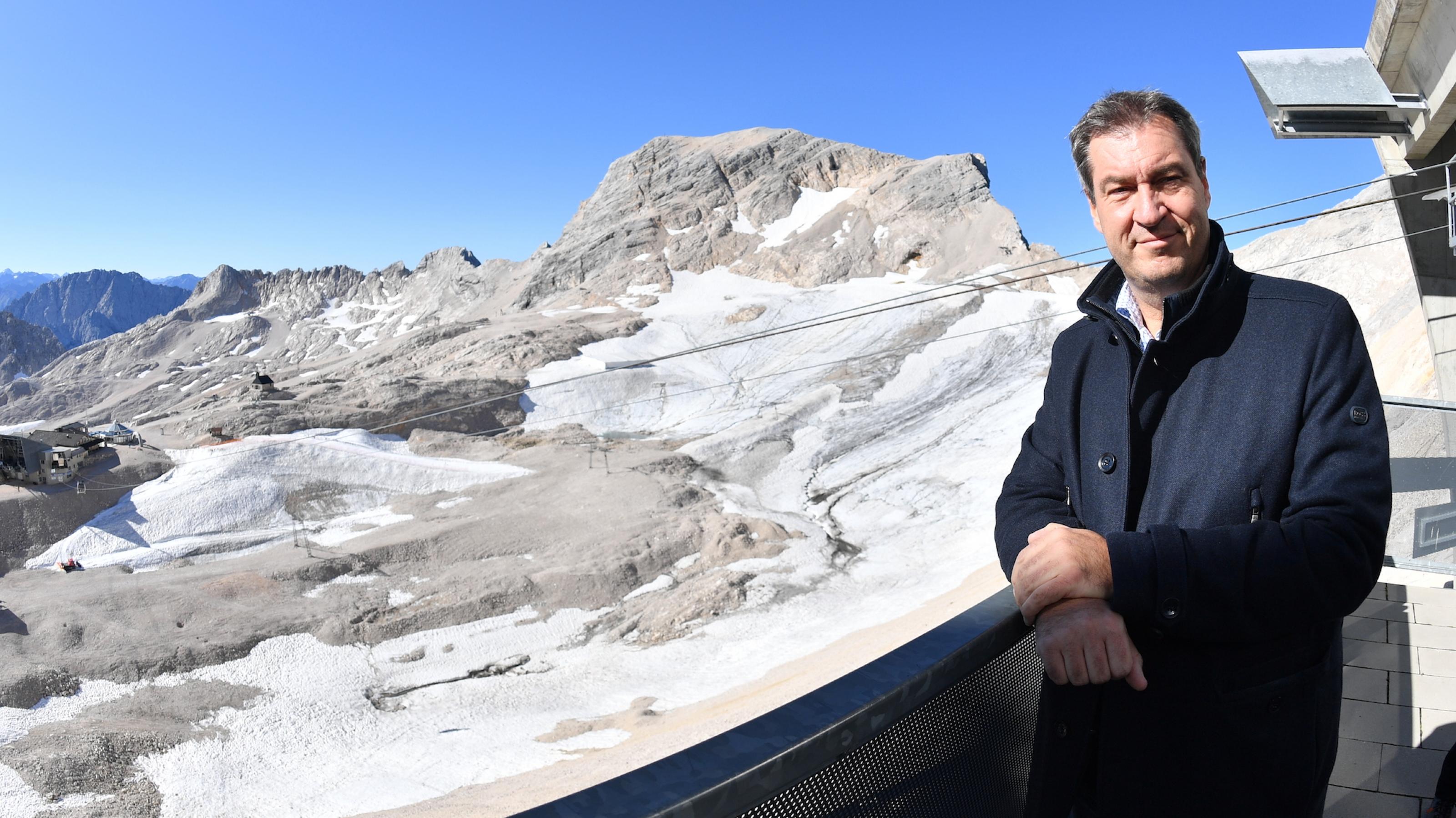 Markus Söder, CSU-Vorsitzender und bayerischer Ministerpräsident, steht rechts im Bild am Geländer eines Balkons und blickt in die Kamera. Hinter und unter ihm ist das Zugspitzplateau mit spärlichem Eis zu sehen. Aufgenommen bei einer Klimatour Anfang September auf der Zugspitze.