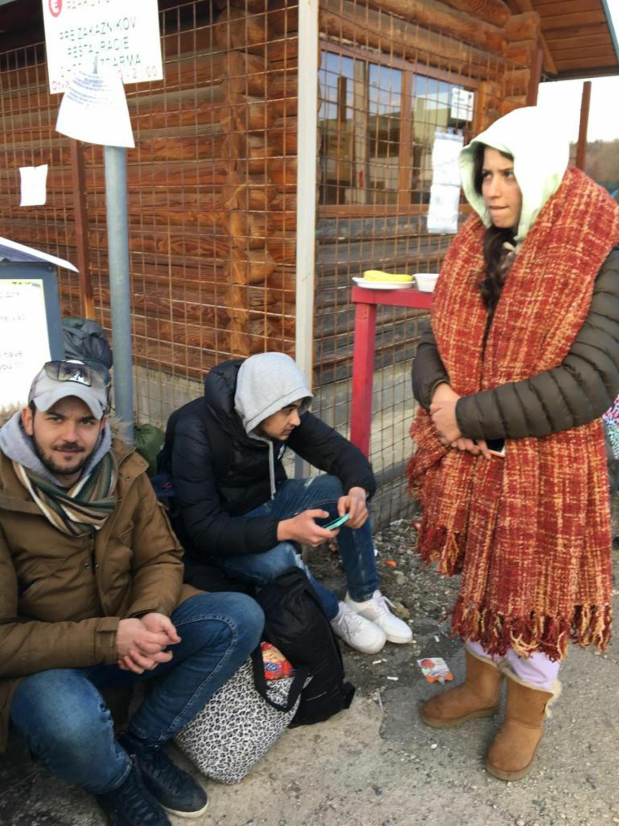 Drei Geflüchtete aus Charkiw in der Ostukraine sitzen und stehen warm bekleidet an einem Häuschen an der slowakischen Grenze
