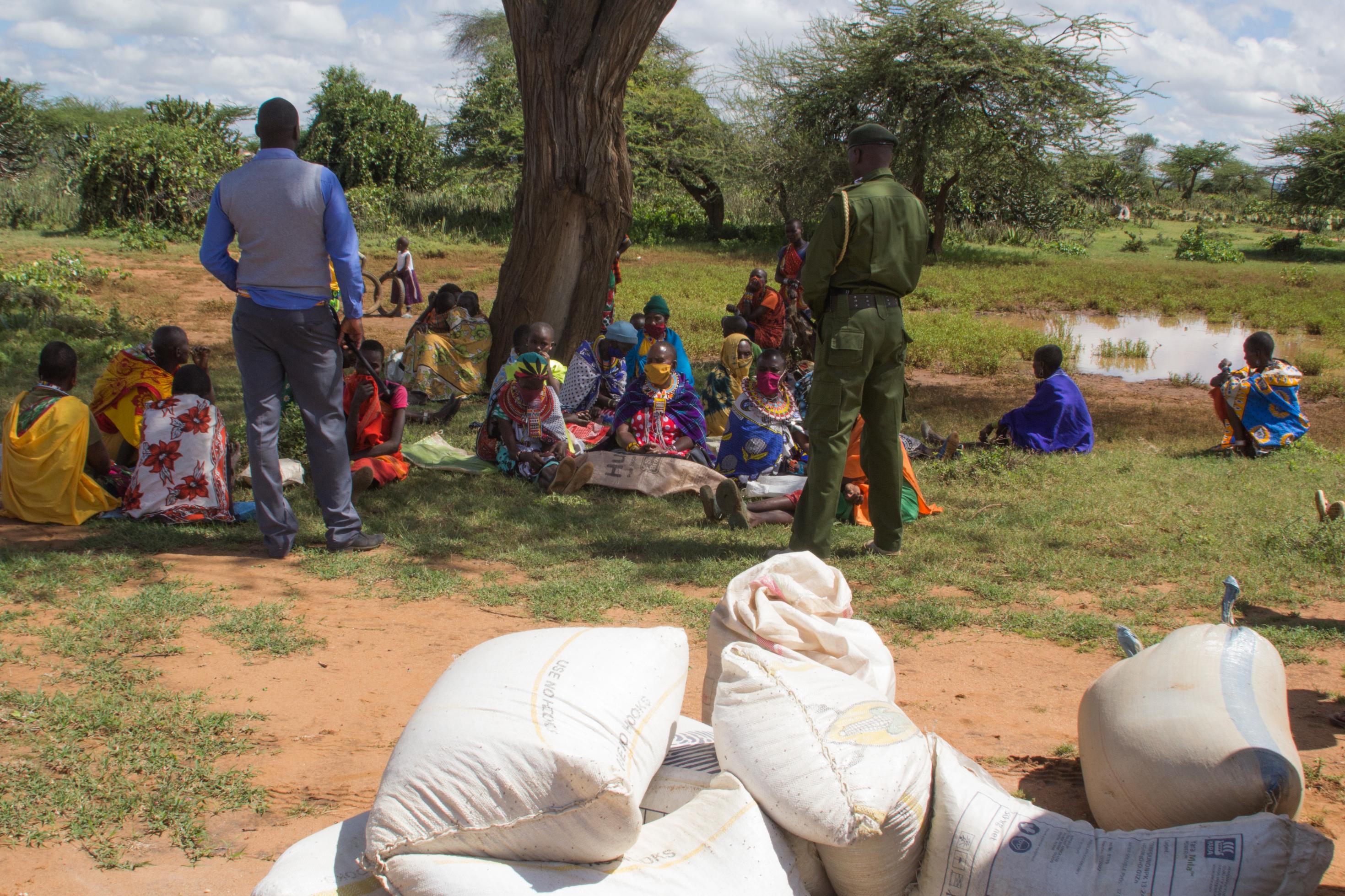Im Schatten eines Baumes sitzen einige Maasai-Frauen im Gras. Sie haben Säcke dabei, sie warten auf die Verteilung der Lebensmittel, die nun in den Schulen nicht ausgegeben werden können.