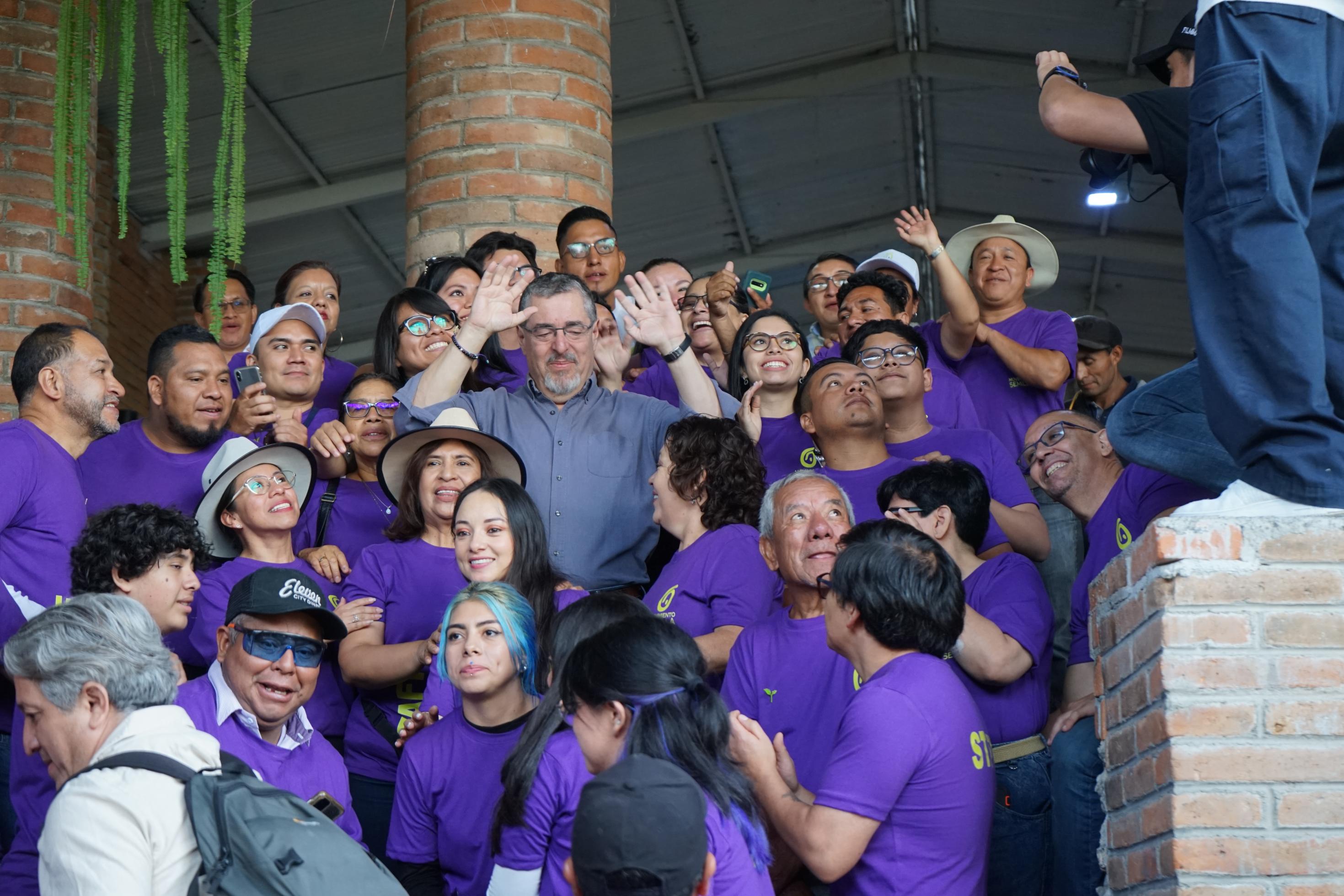 Arévalo winkt in die Kamera, umgeben von lila gekleideten hauptsächlich jungen Leuten.