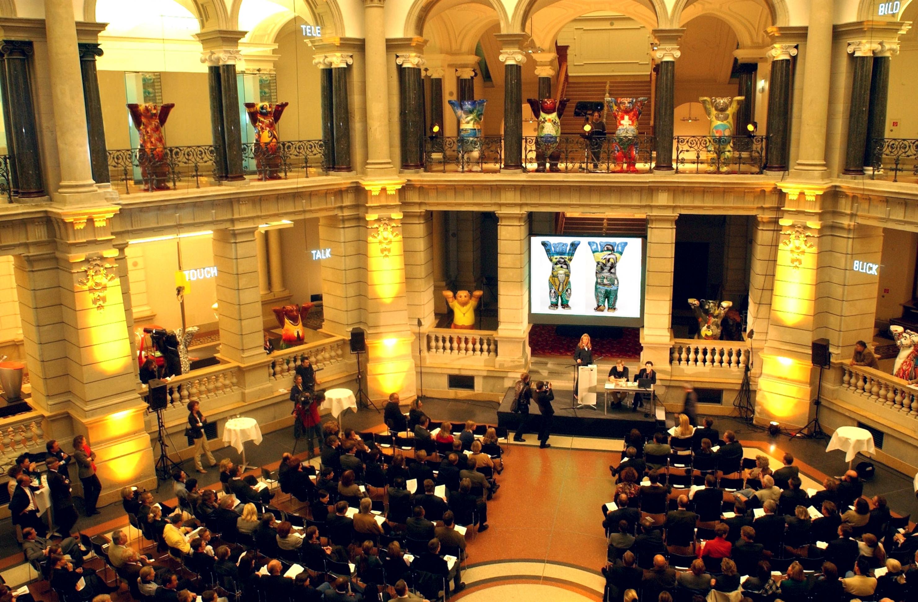 Blick in den Lichthof des Museums für Kommunikation in Berlin, in dem dieses Zukunftsszenario spielt. Zu sehen ist eine Versteigerung von Buddy-Bären.