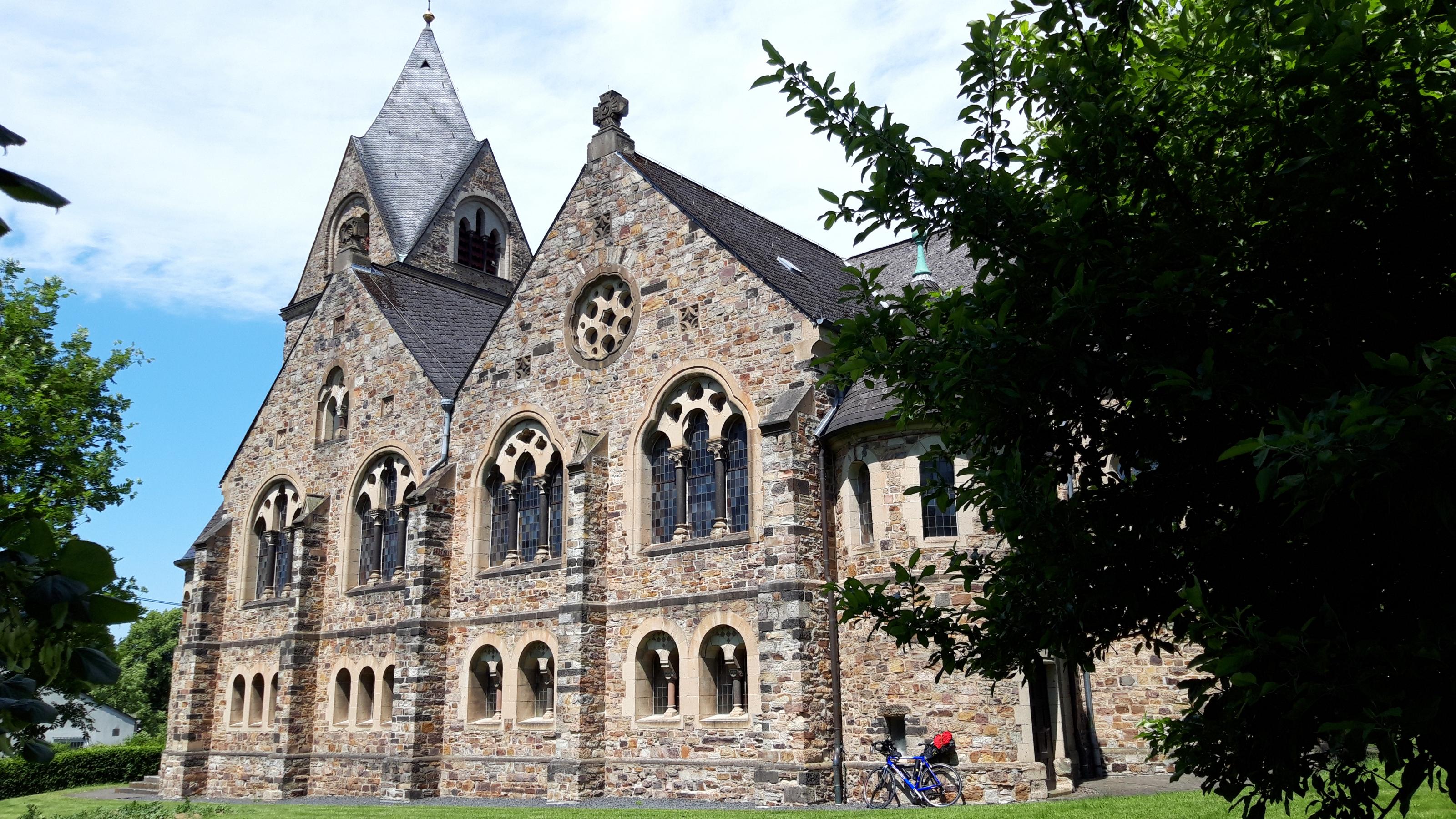 Das Vehikel des RadelndenReporters lehnt an der Evangelischen Pfarrkirche Dierdorf, eine neuromanische Staffelkirche aus den Jahren 1903 bis 1904 mit spätromanischem Westturm.