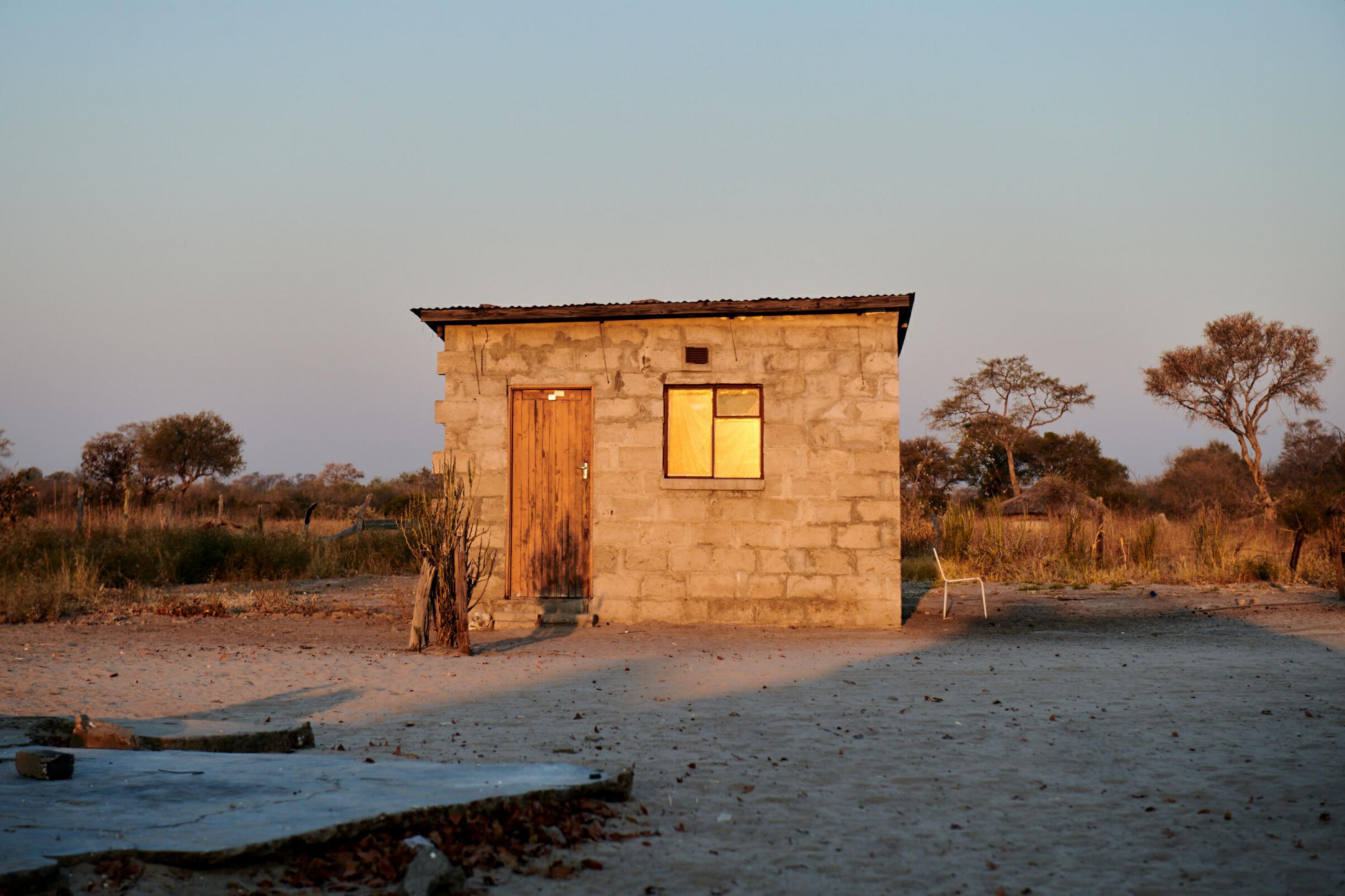 Ein kleines Steinhaus mit Holztür steht in der weiten Landschaft des Dorfes, daneben steht ein Stuhl im Schatten